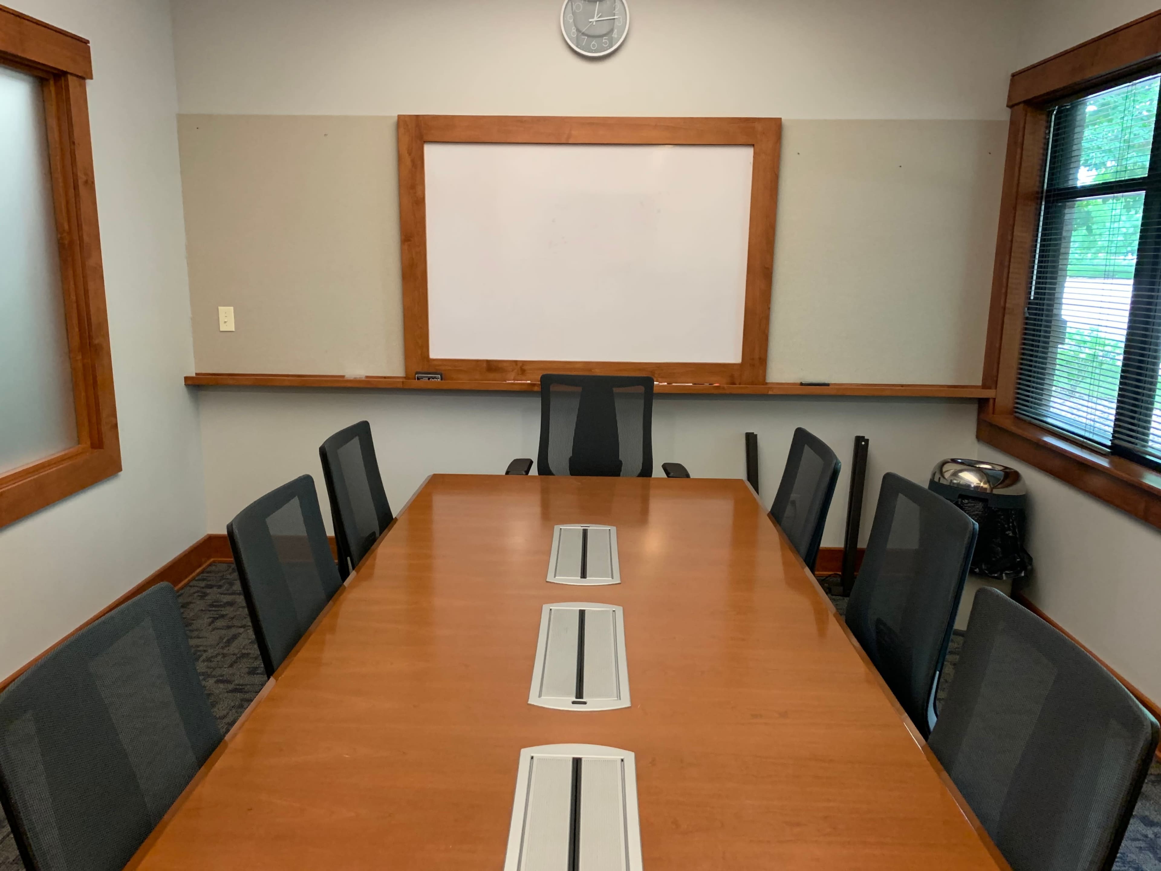 A conference room with a large wooden table surrounded by several black chairs and a whiteboard on the wall.