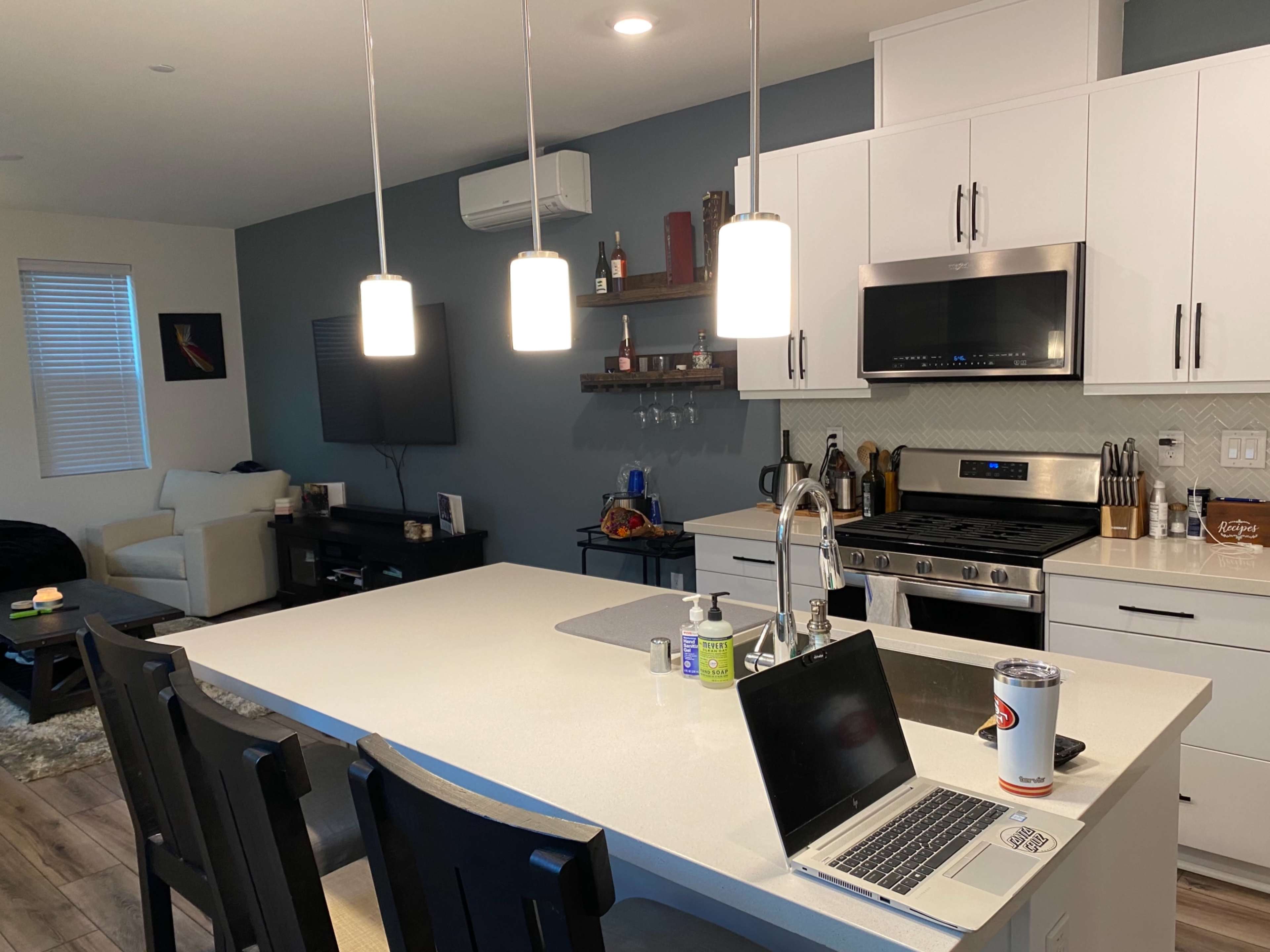 A modern kitchen features white cabinetry, a large island with bar seating, and a living area with a couch and television in the background.