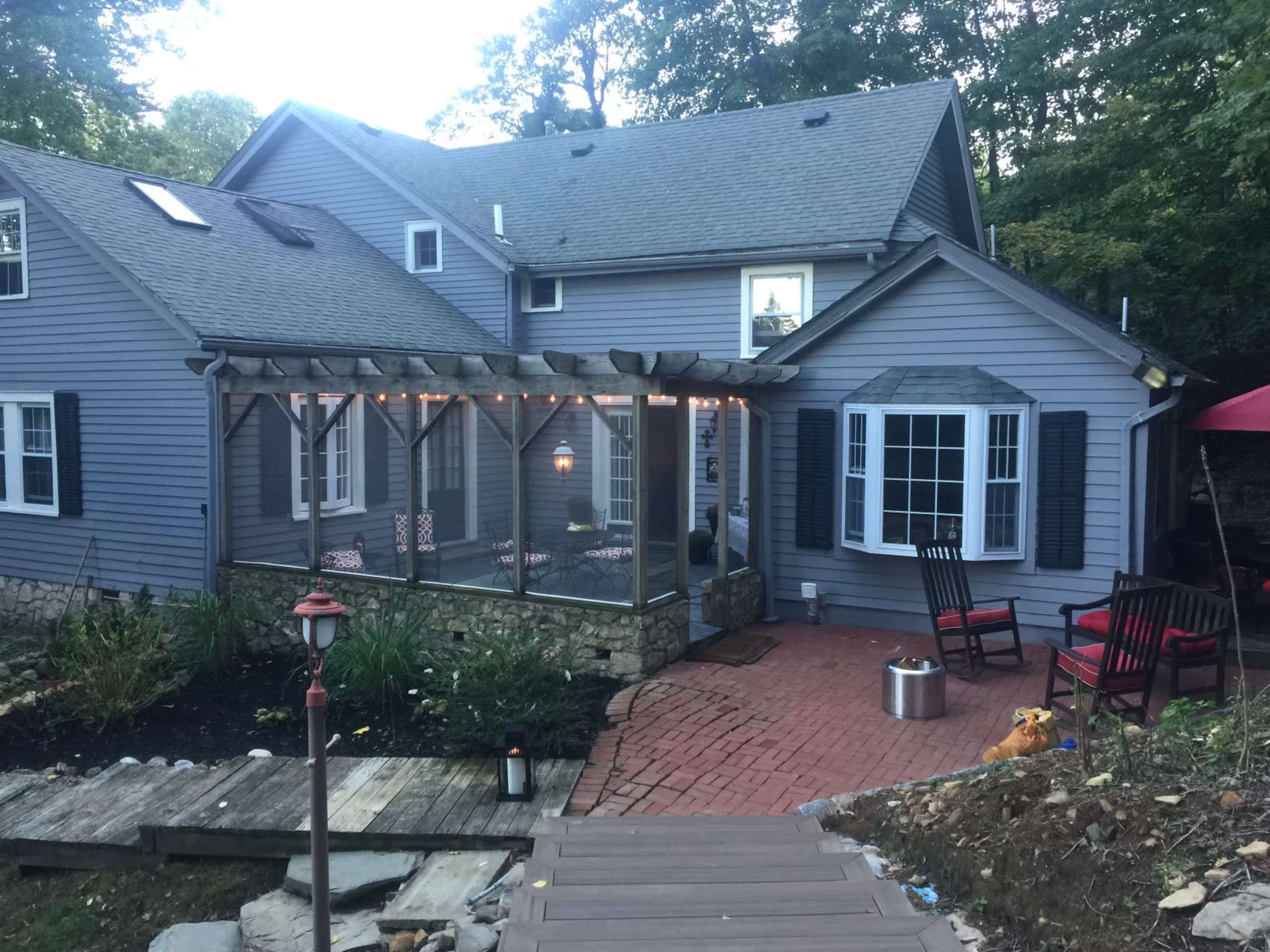 A gray house with a screened-in porch, surrounded by trees, a brick patio, and outdoor seating.