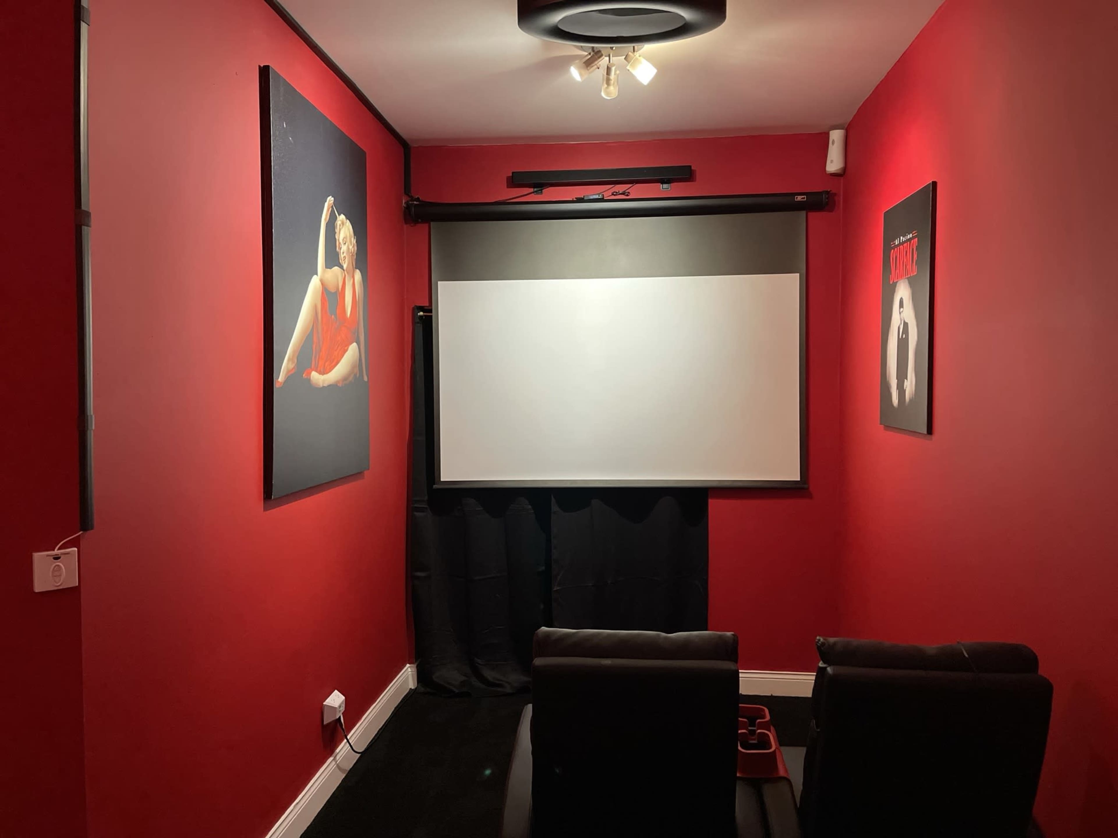 A home theater room with red walls, a projection screen, and black leather seating.
