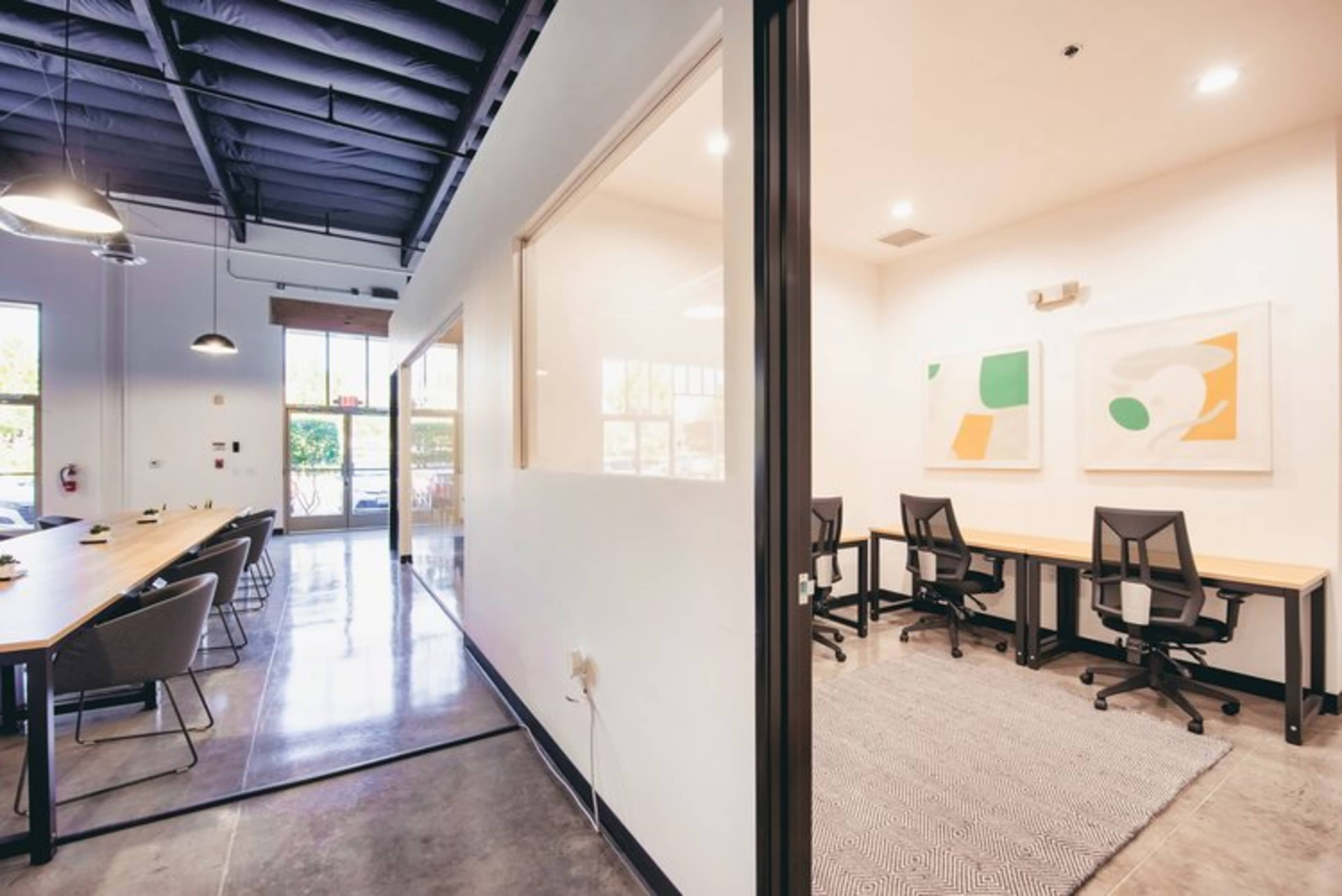 A modern office space with a corridor leading to a meeting room and an adjoining workspace featuring minimalistic furniture and large windows.