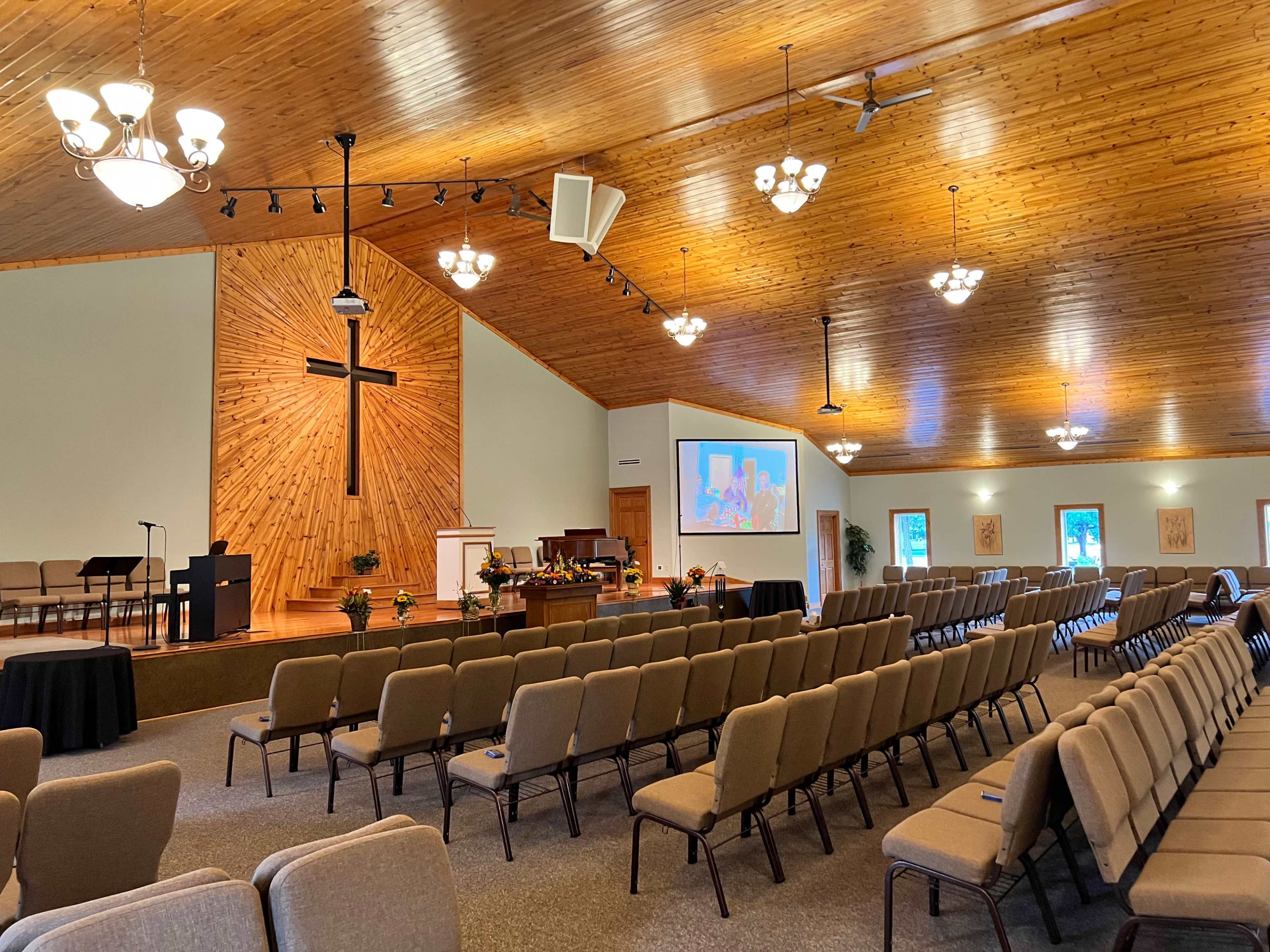 The interior of a church with rows of chairs facing a stage that features a large cross and a projection screen.