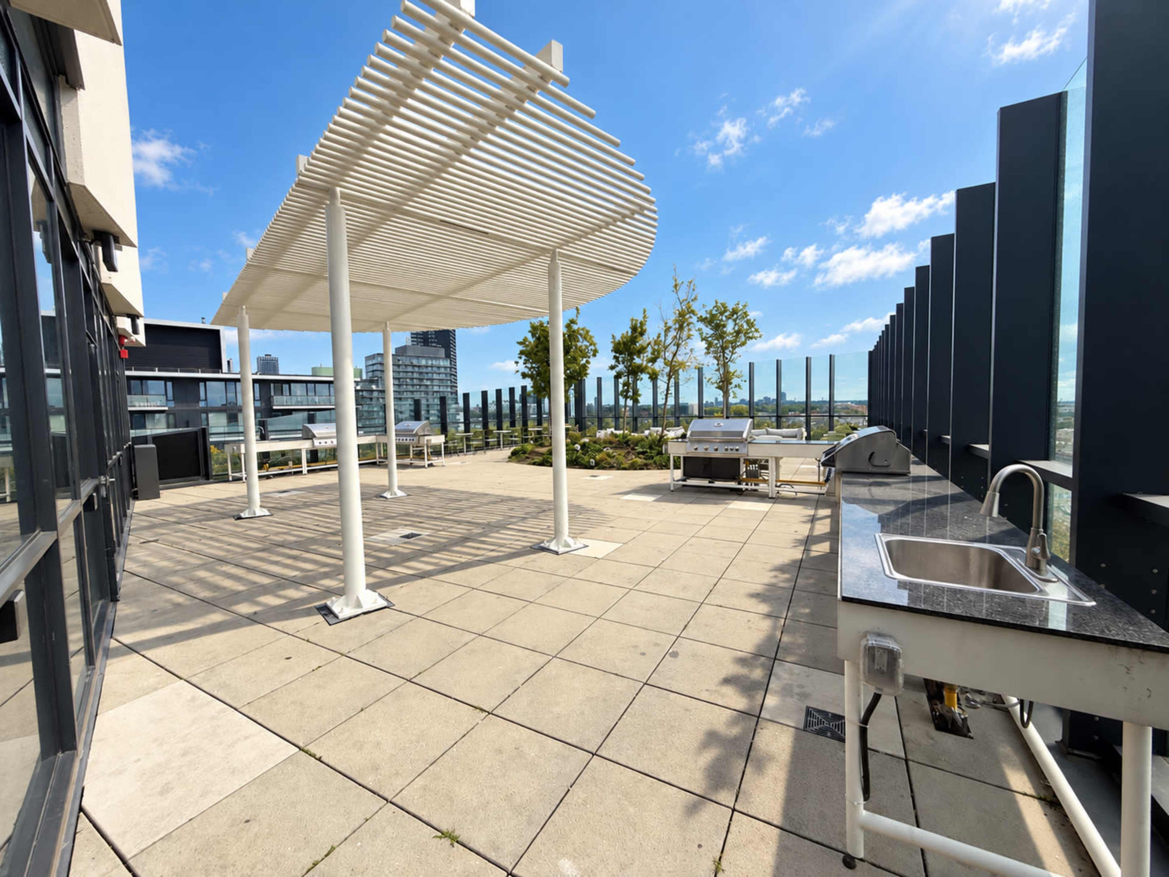 The image shows a spacious rooftop terrace featuring a shaded area, several small trees, and outdoor cooking facilities.