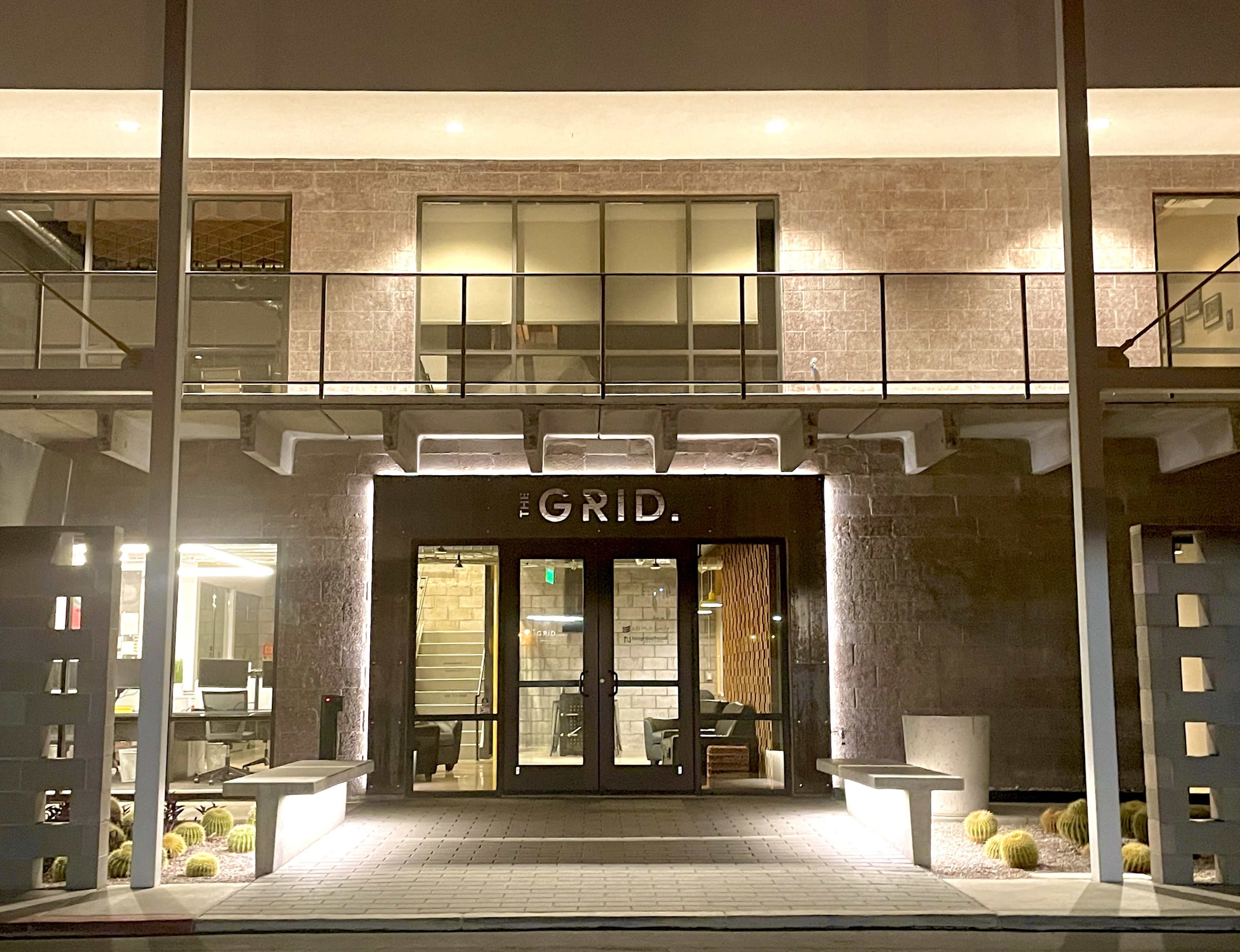 The image shows the entrance of a building labeled "THE GRID" with modern architecture and illuminated features at night.
