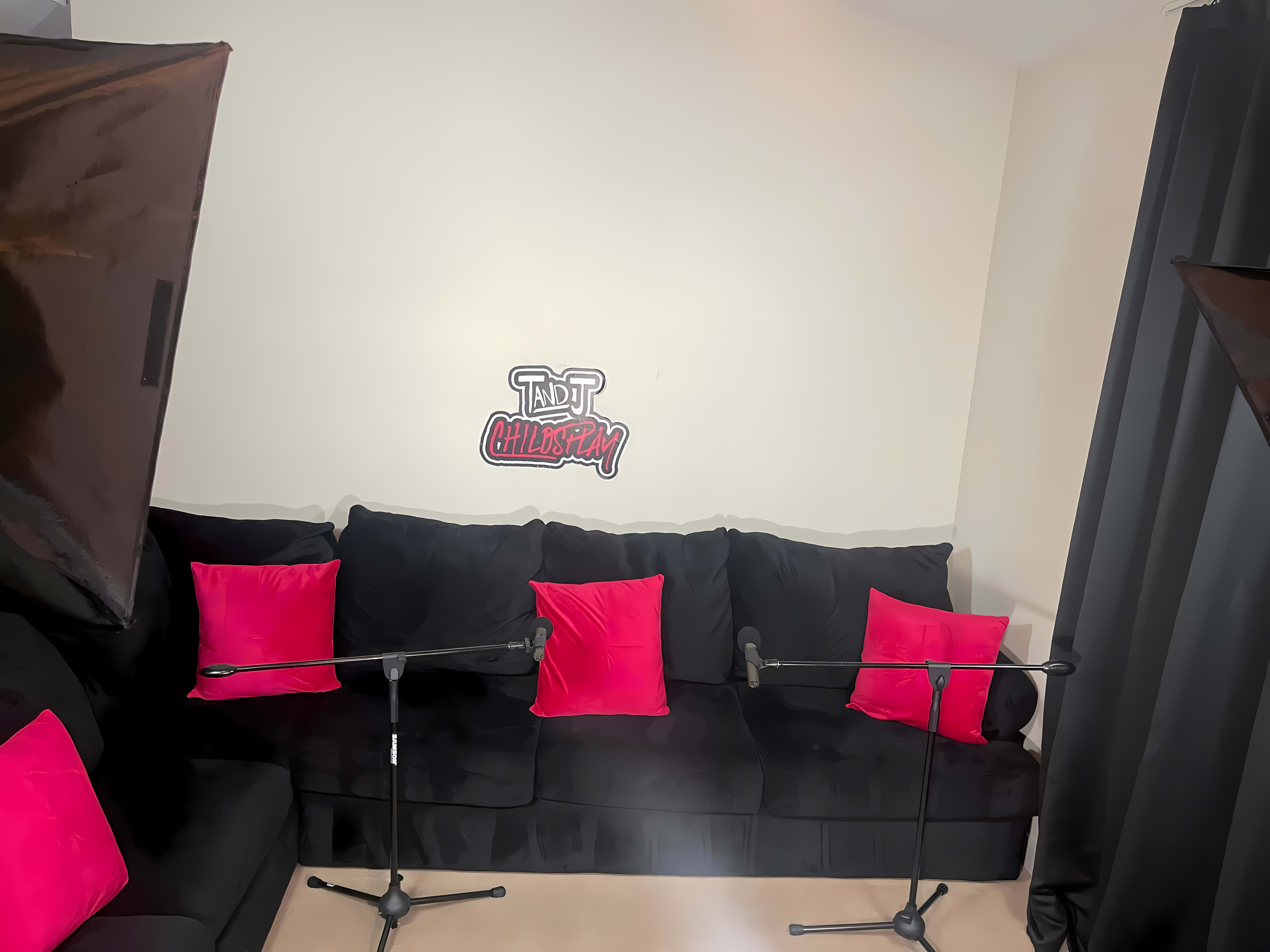 A black couch with pink pillows, two microphones positioned in front of it, and a wall featuring a logo that says "TND Chill and Play."