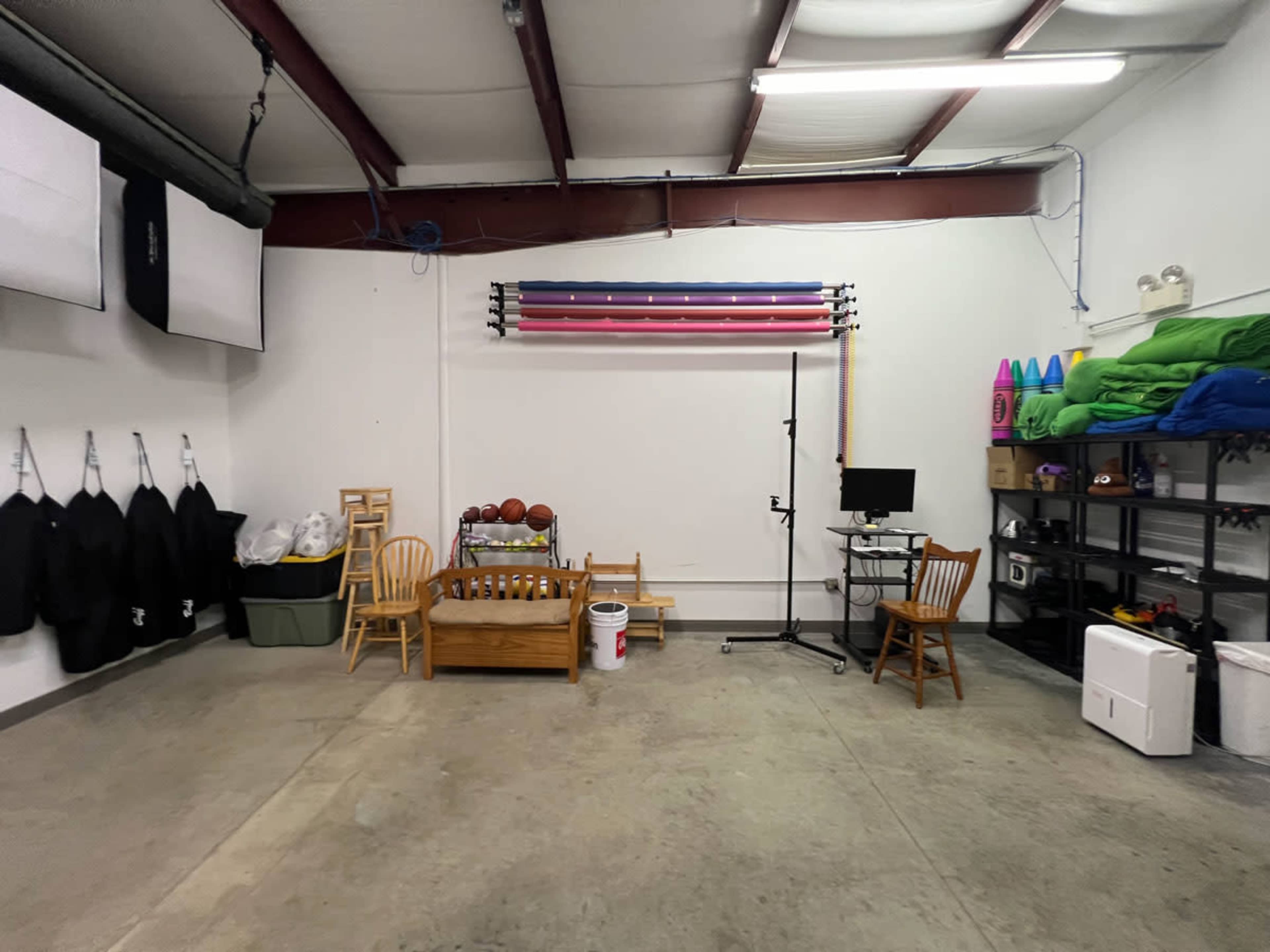 The image shows a spacious garage interior with exercise equipment, storage shelves, chairs, and various gym supplies.