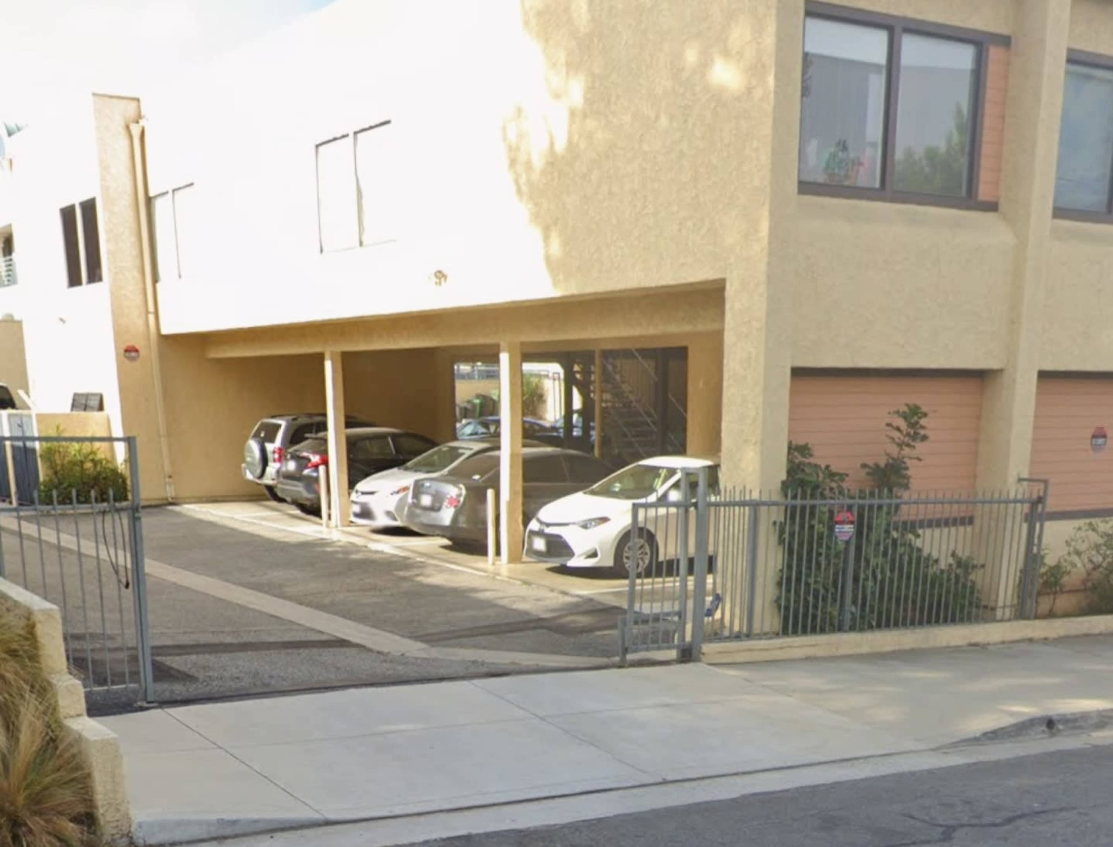 A parking area under a building with several parked cars and a gated entrance.