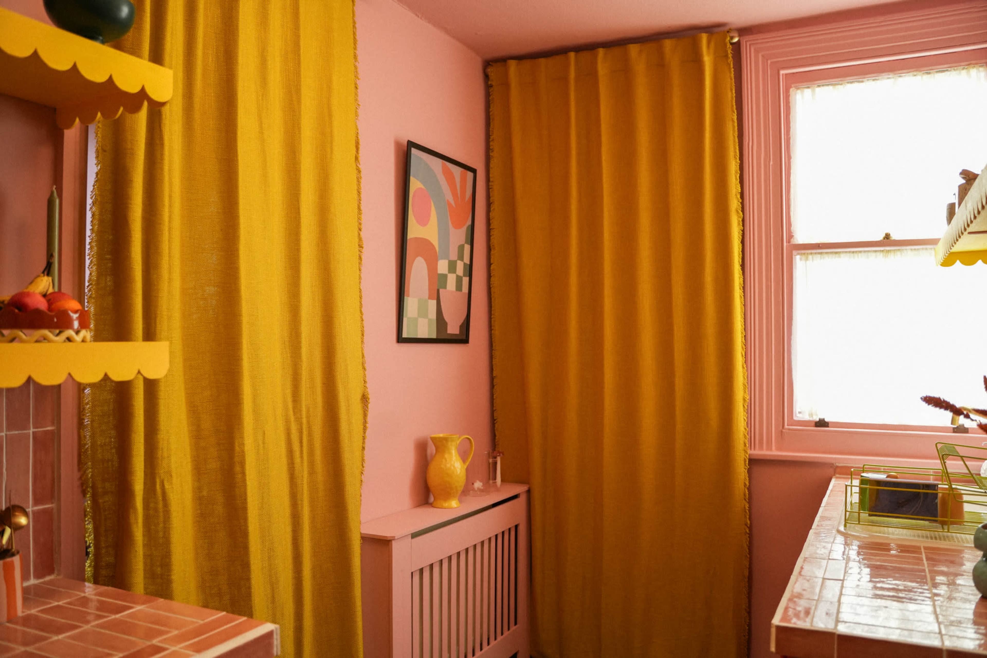 A kitchen corner features pink walls, yellow curtains, and a fruit bowl on a shelf.
