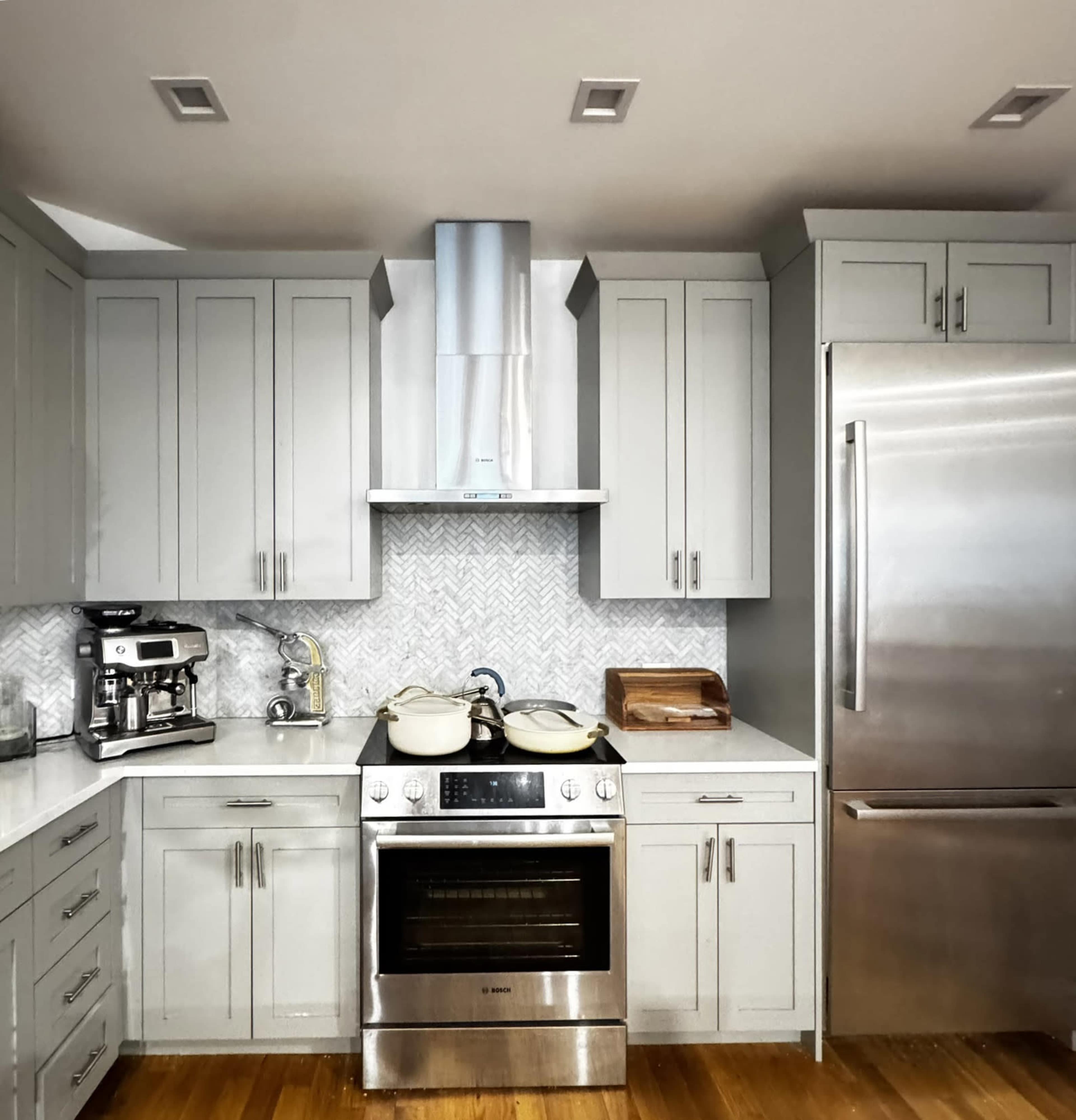 A modern kitchen features gray cabinetry, stainless steel appliances, and a marble-patterned backsplash.