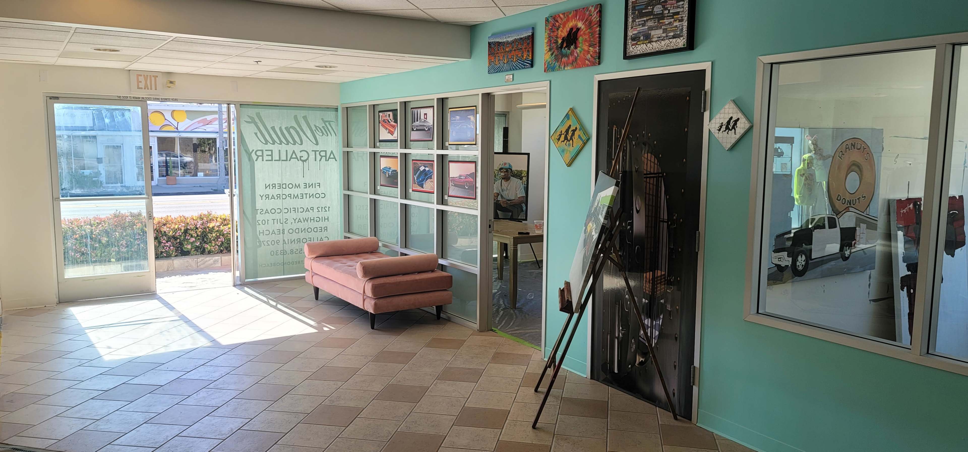 A brightly lit art gallery entrance with a pink sofa on the left and framed artwork displayed on the walls.