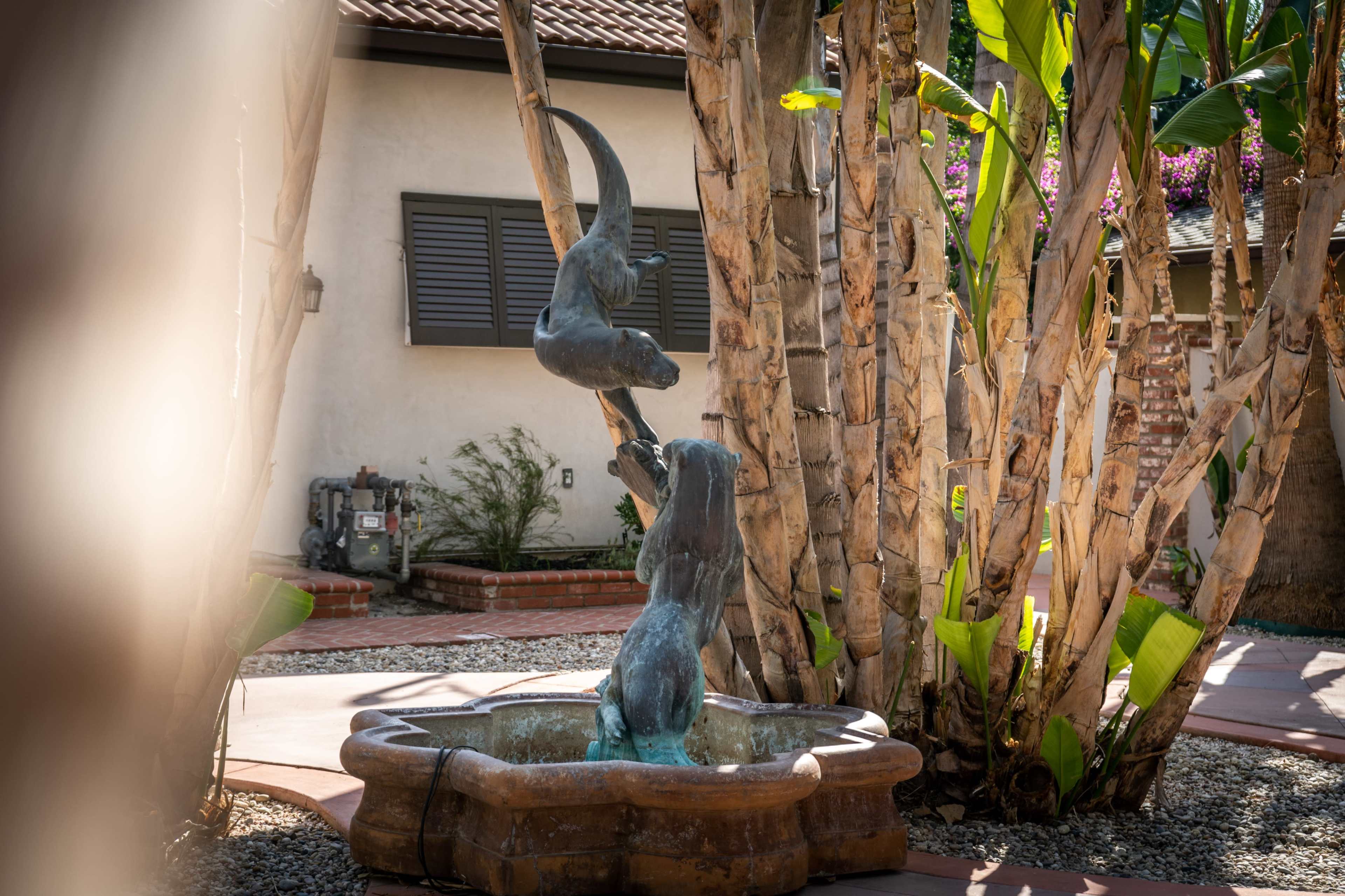 A bronze fountain featuring two playful monkeys is surrounded by palm trees and a landscaped yard.