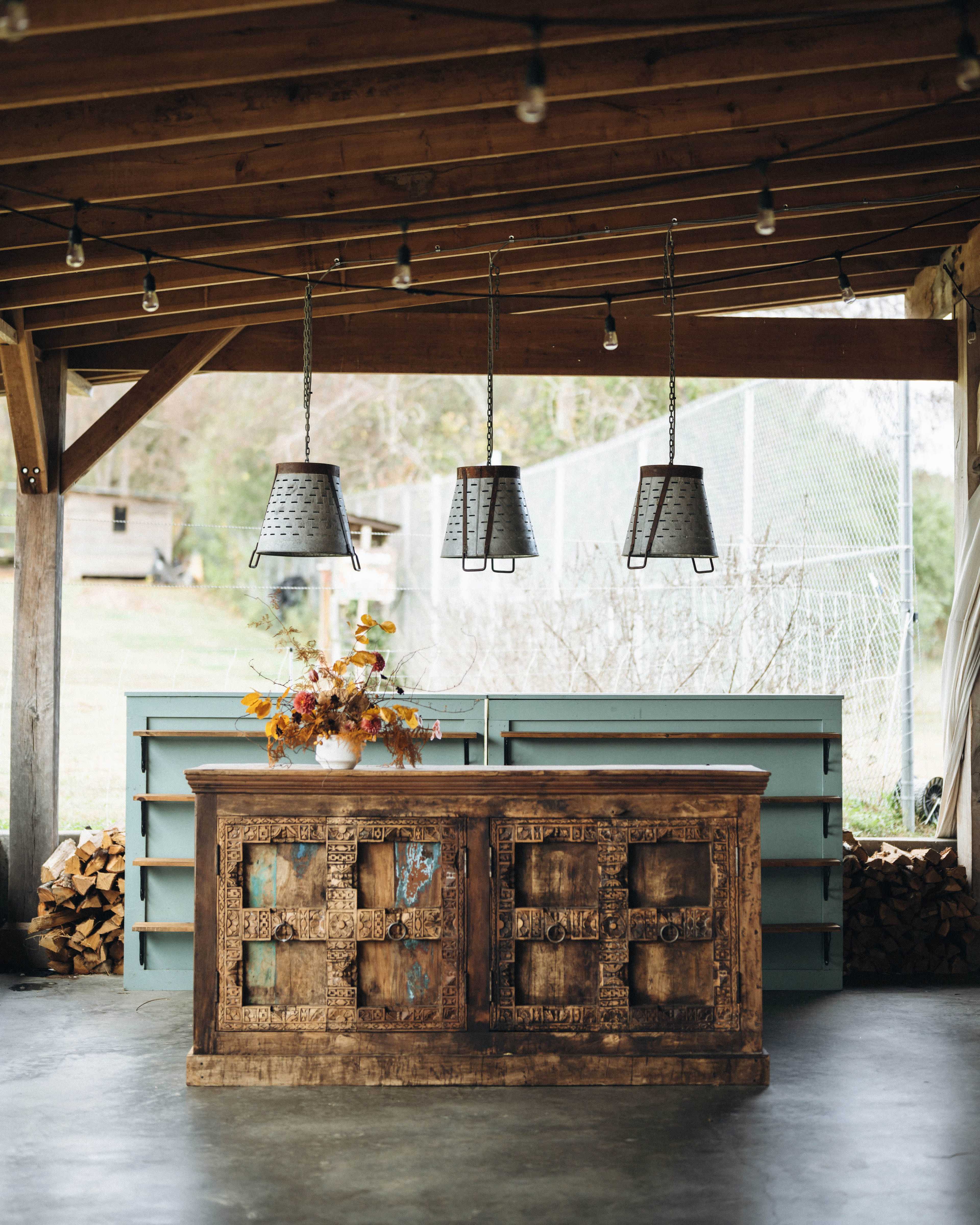A rustic wooden counter with intricate carvings is set beneath hanging industrial-style light fixtures in a spacious open area.