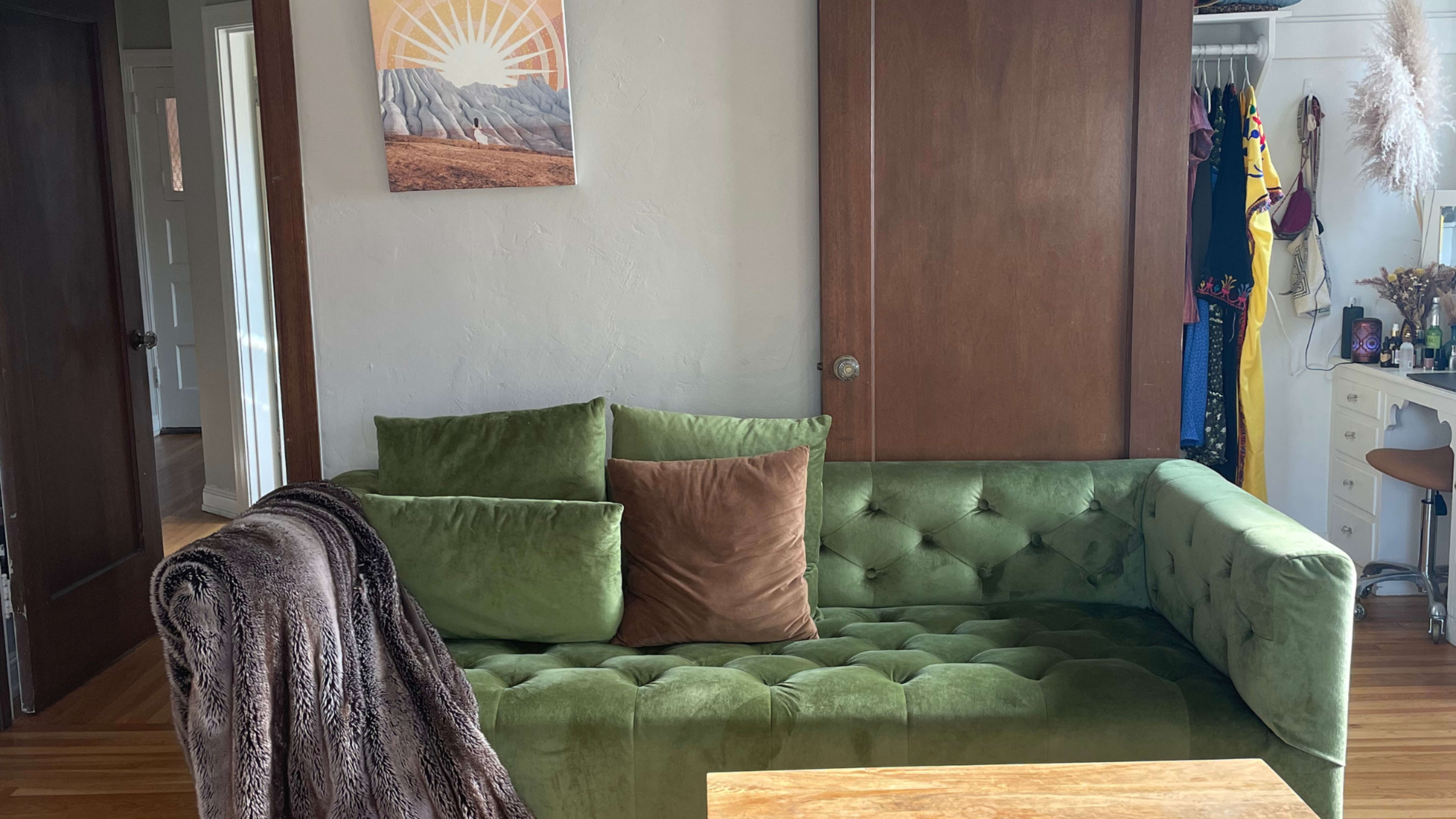 A green tufted couch sits in a room with wooden doors and a painting of mountains on the wall.