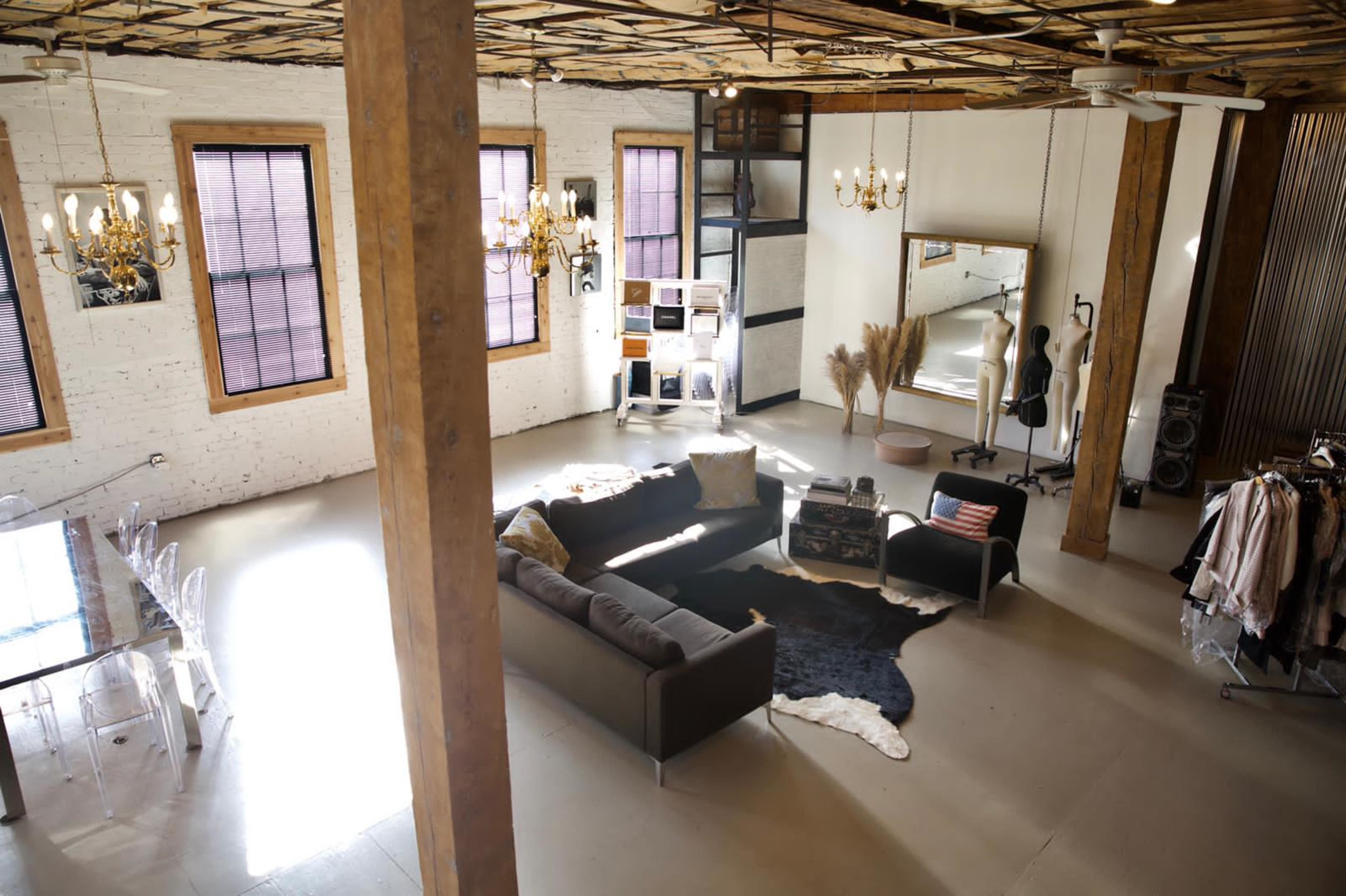 A spacious room with exposed wooden beams, large windows, a sofa, decorative elements, a dining area, and a mirror reflecting the interior.