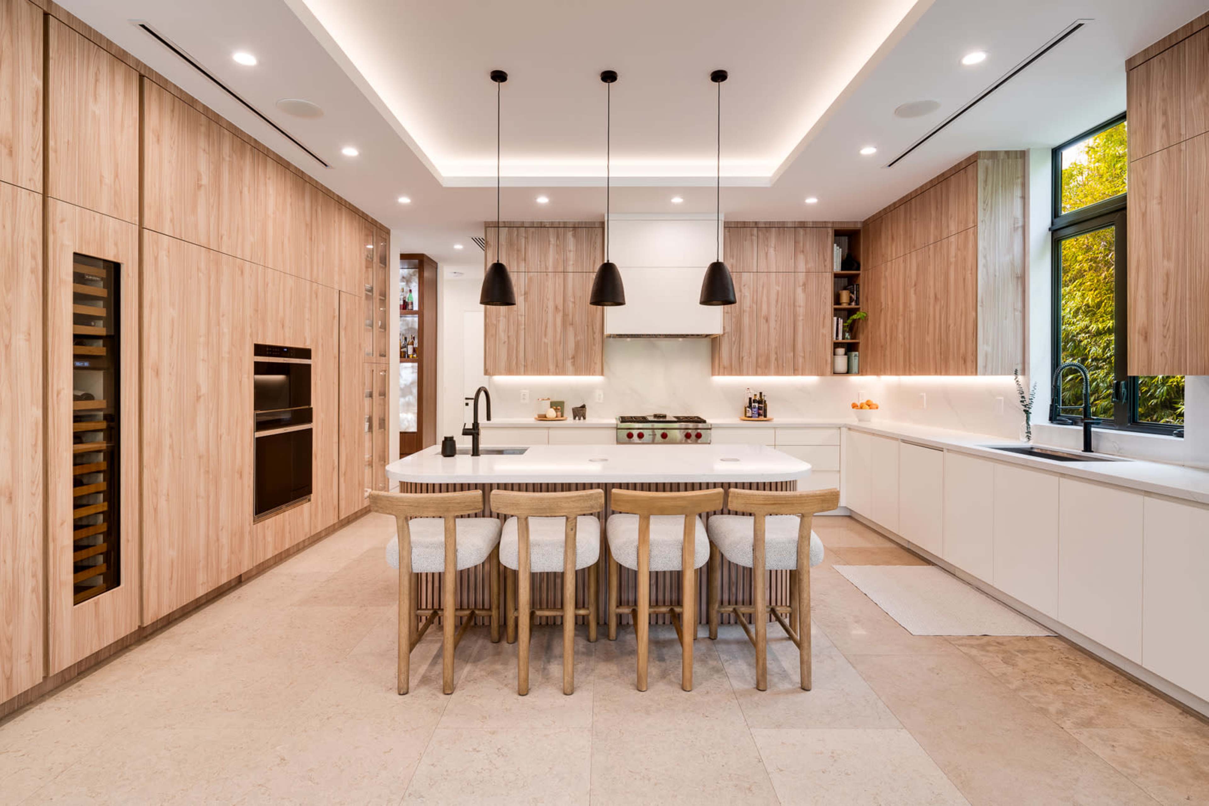 A modern kitchen features sleek cabinetry, a large island with seating, and pendant lighting.