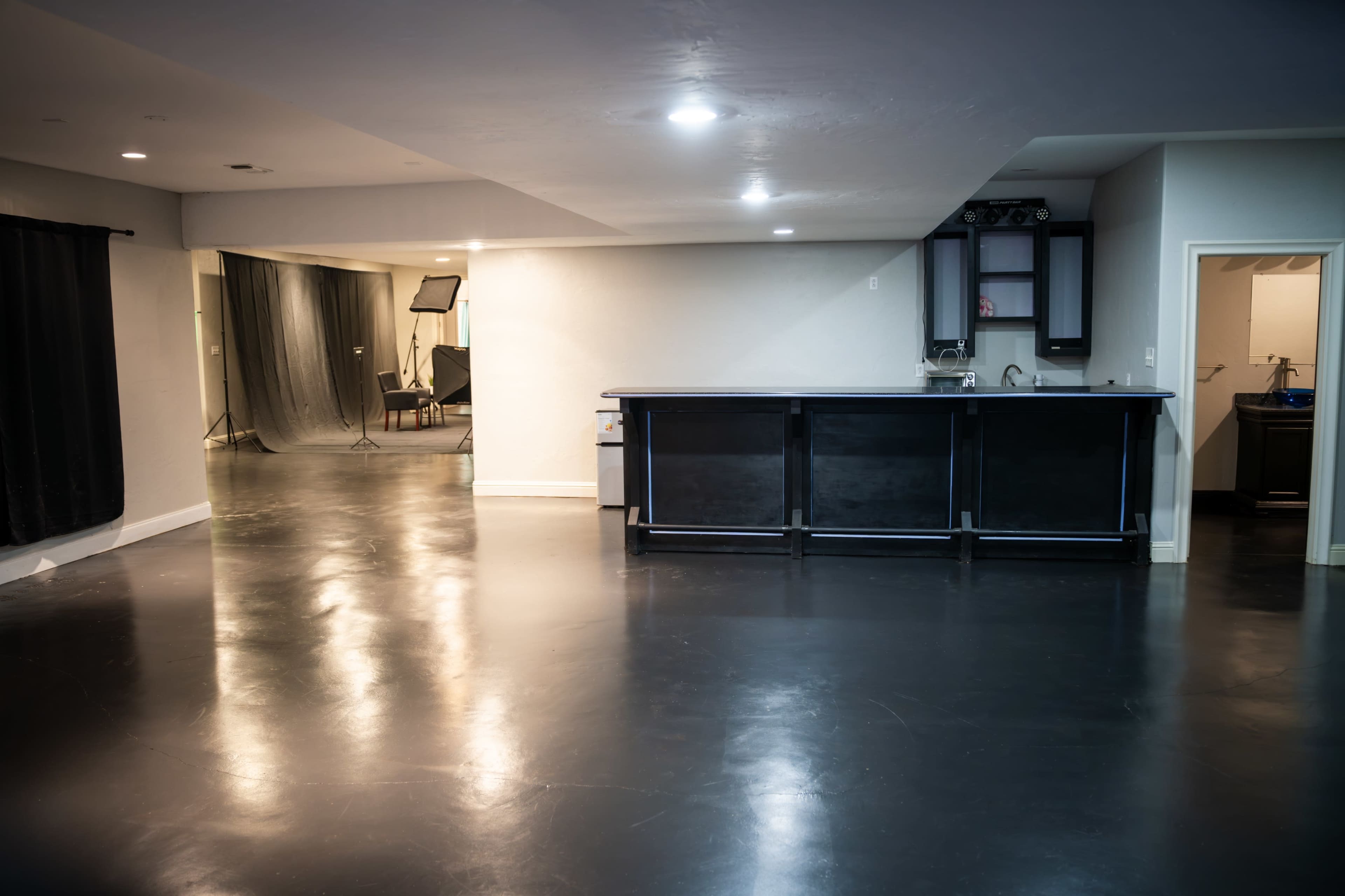 A spacious room with a polished black floor, featuring a bar area and a doorway leading to a separate space.