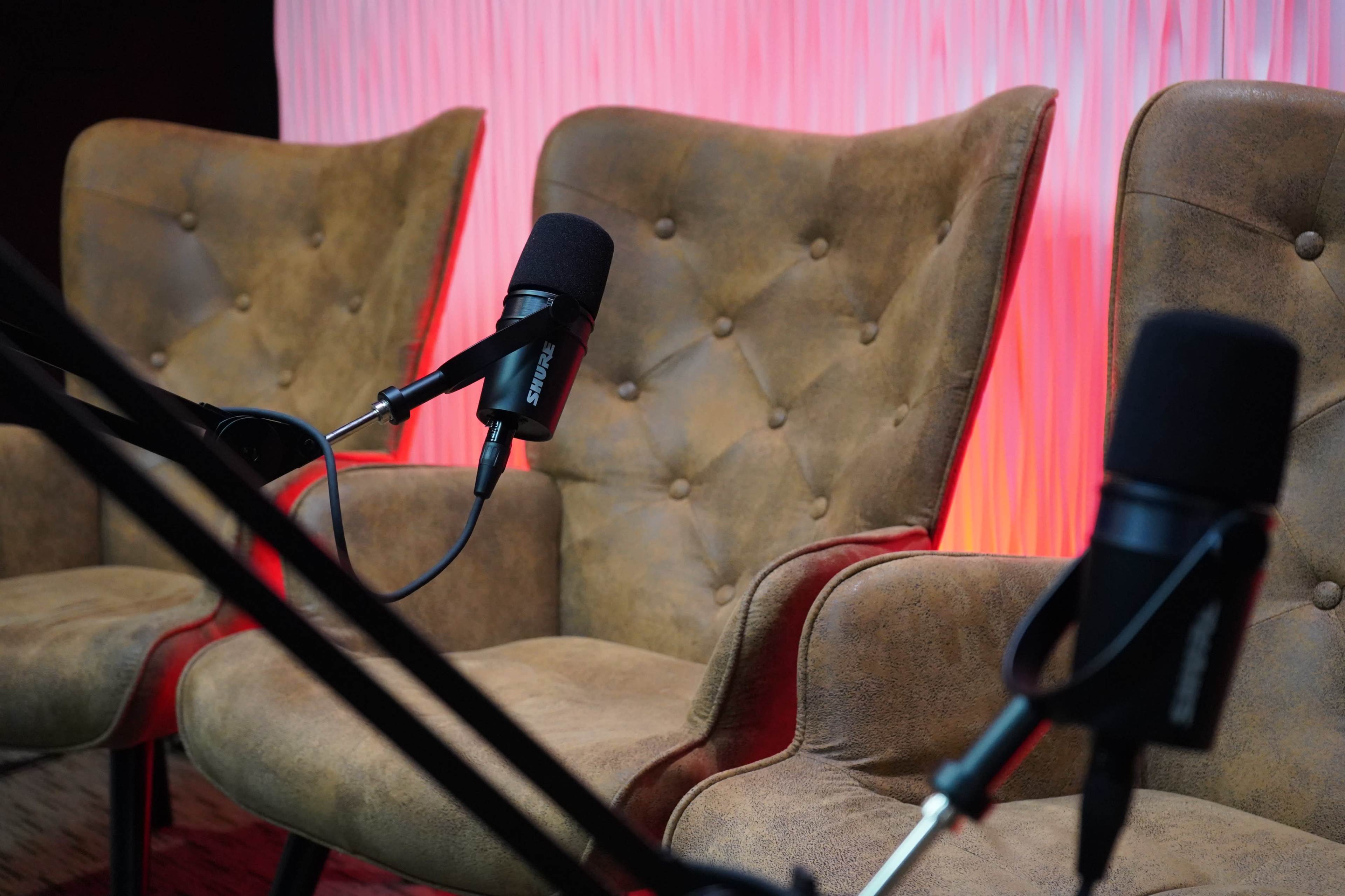The image shows two plush armchairs with microphones positioned in front of them, set against a softly lit, textured background.