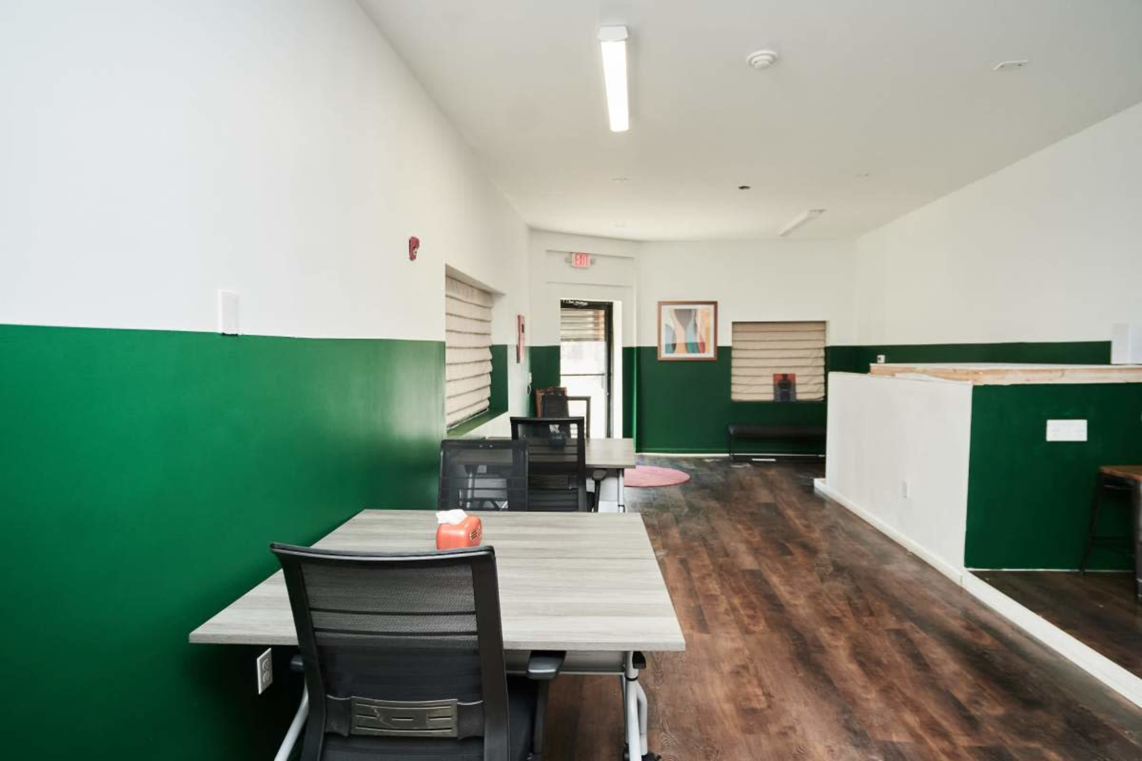 An indoor office space featuring green and white walls, wooden flooring, and several work desks arranged along one side.