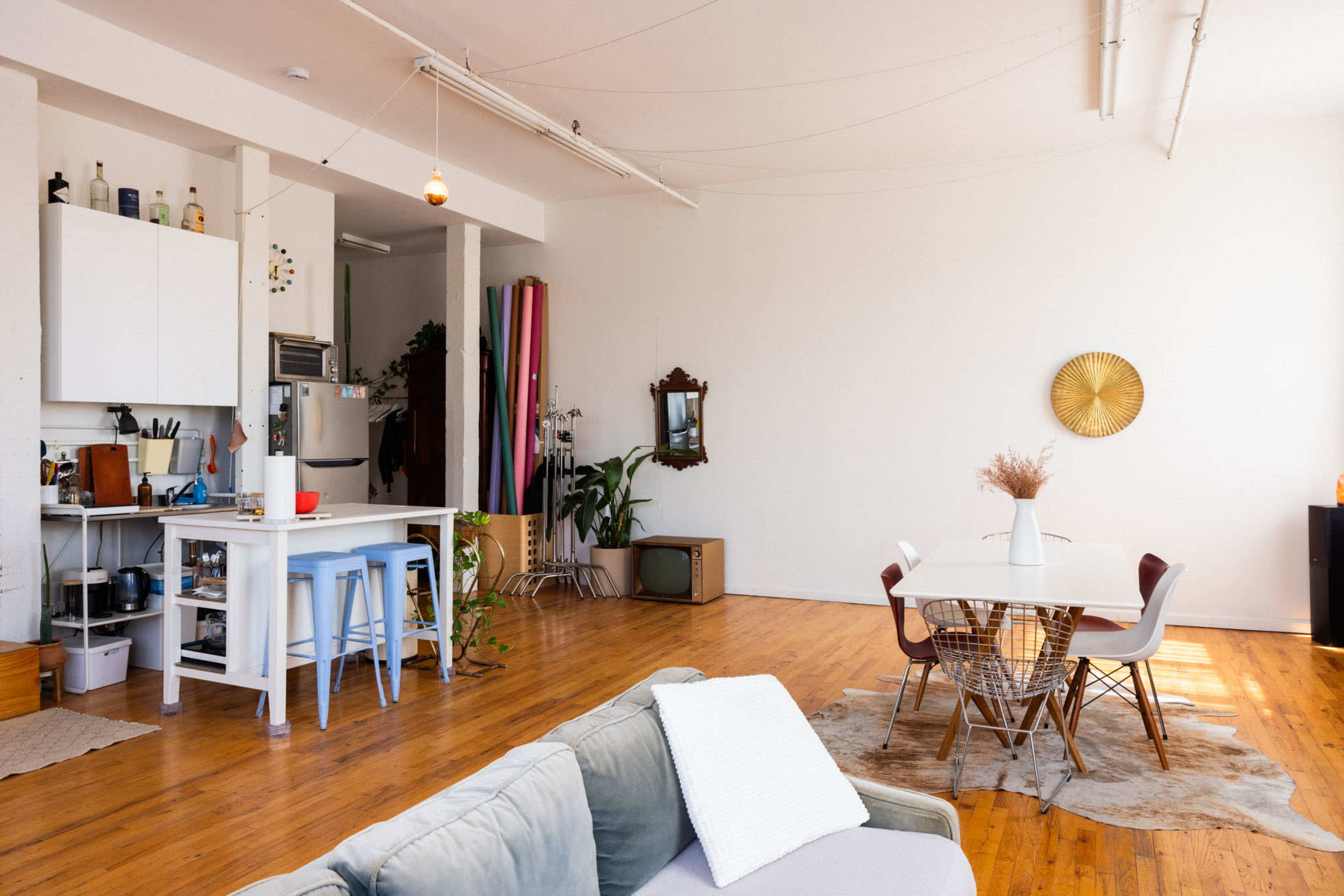 A spacious, well-lit room features a dining area with a round table and chairs, alongside a kitchen counter with bar stools, all situated on wooden floors.