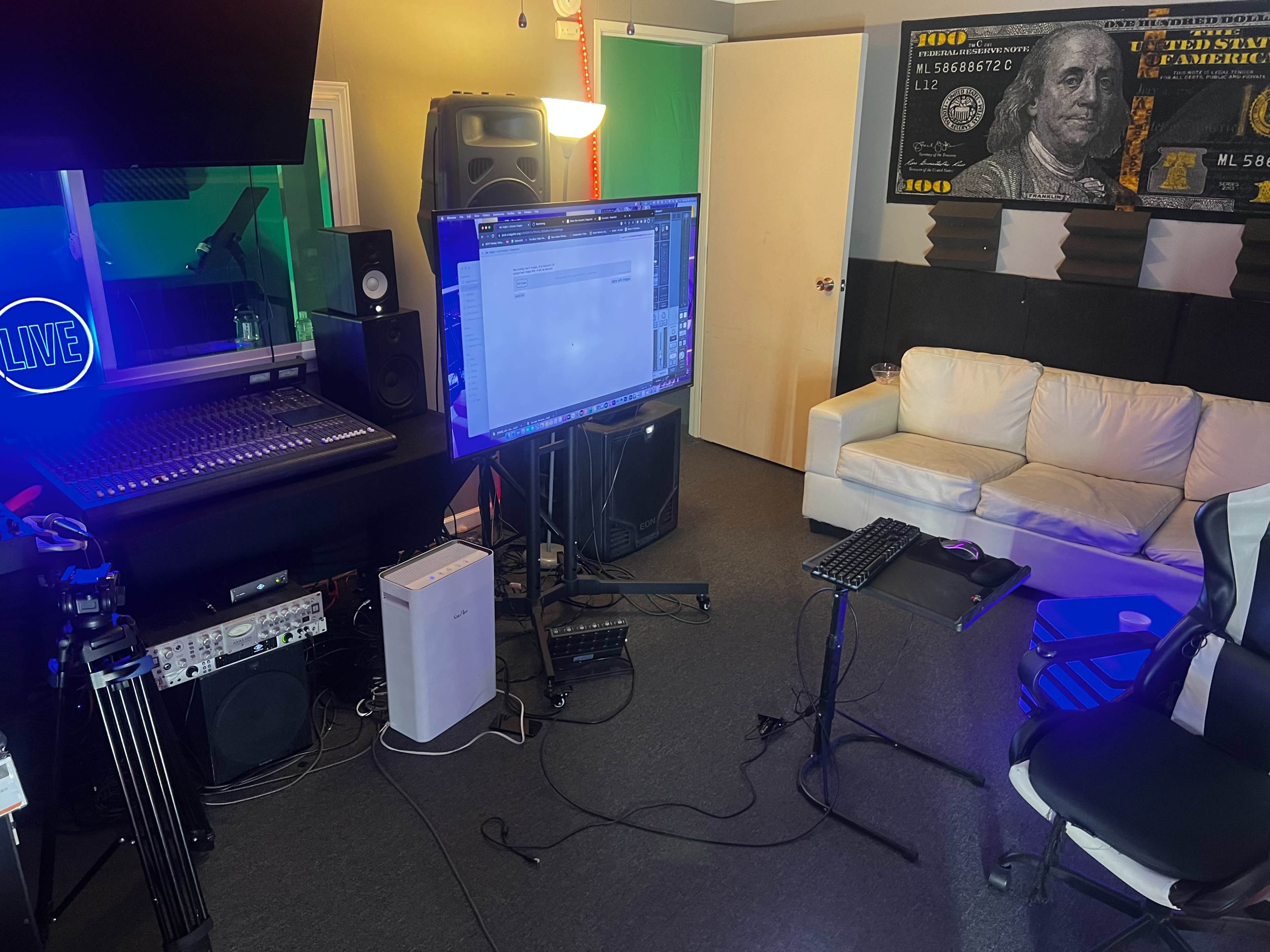 The image shows a music production studio with a mixing console, speakers, a large monitor, and a couch, all arranged in a dimly lit space.