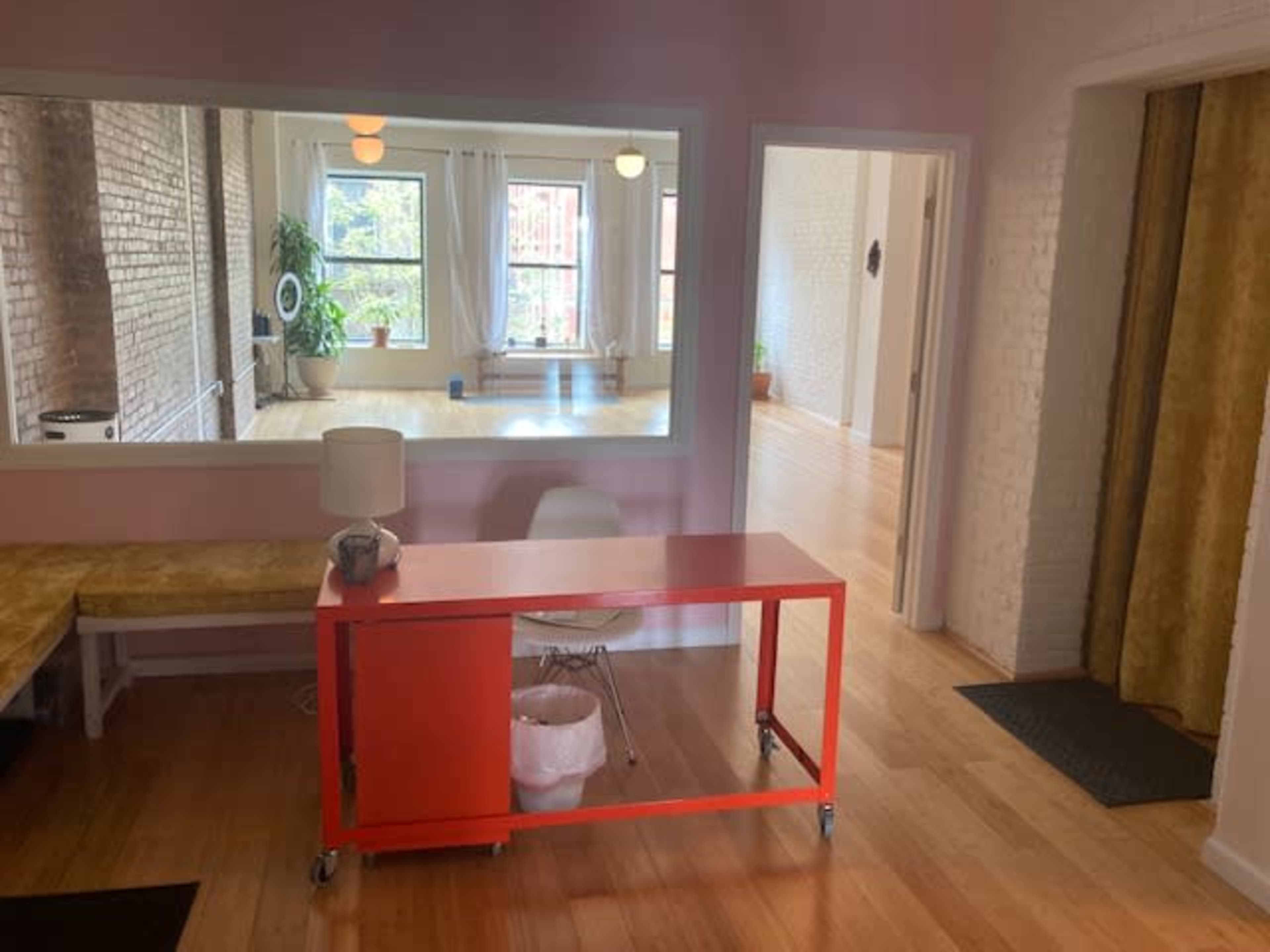 A spacious, well-lit room with hardwood flooring, featuring a red table and a mirror that reflects another area of the room.