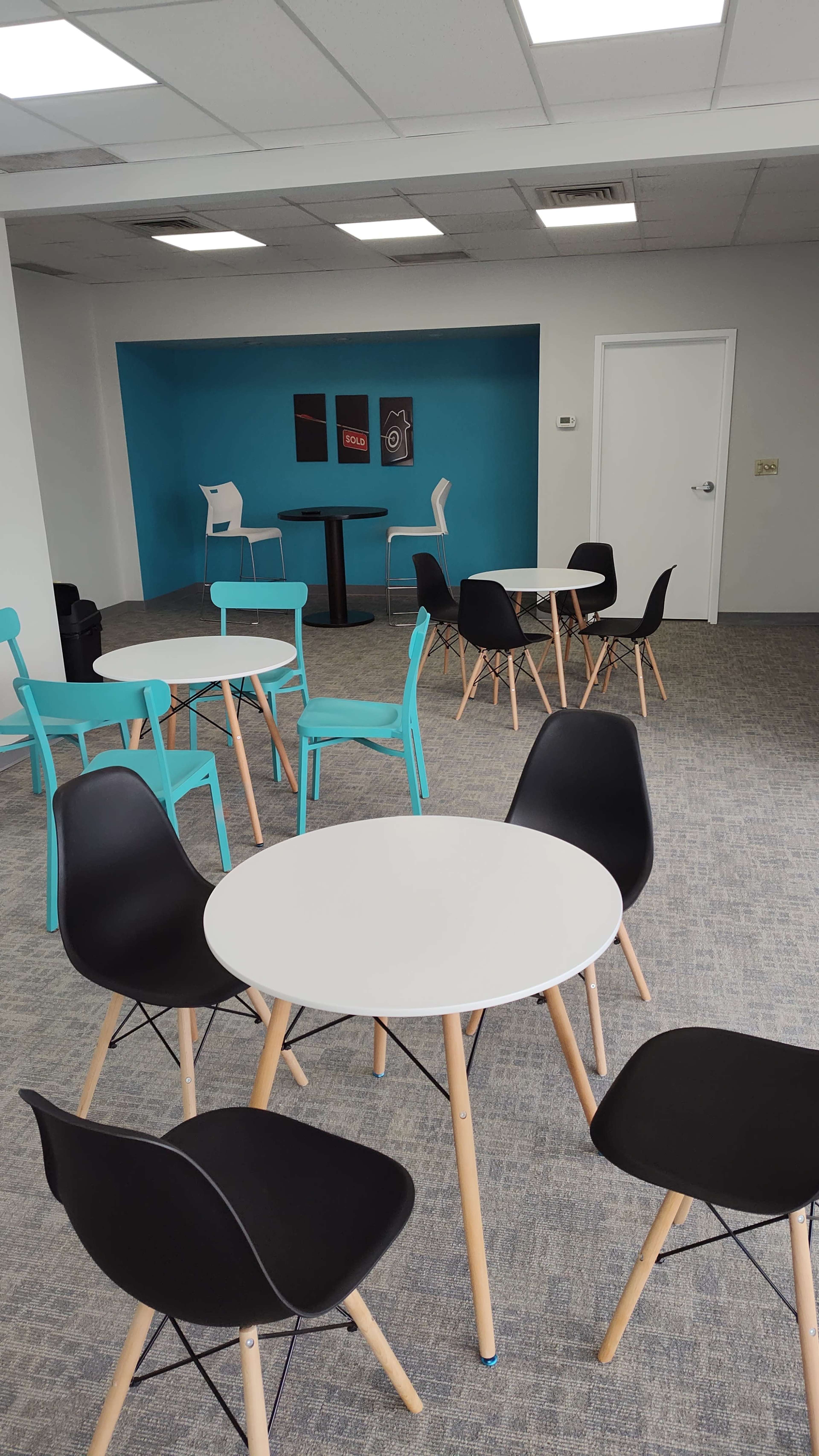 The image shows a modern office break area with several tables and chairs arranged in a bright, open space.