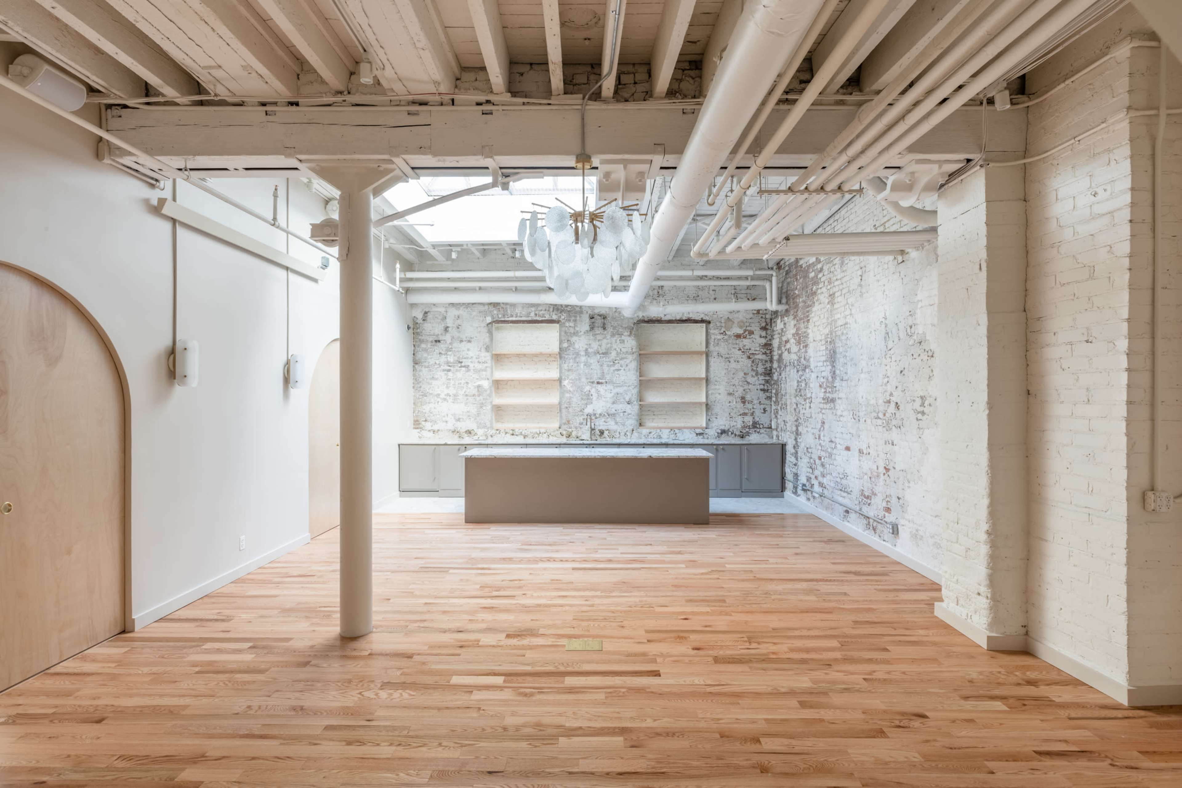 A spacious, light-filled room with wooden floors, exposed brick walls, and a central kitchen island.