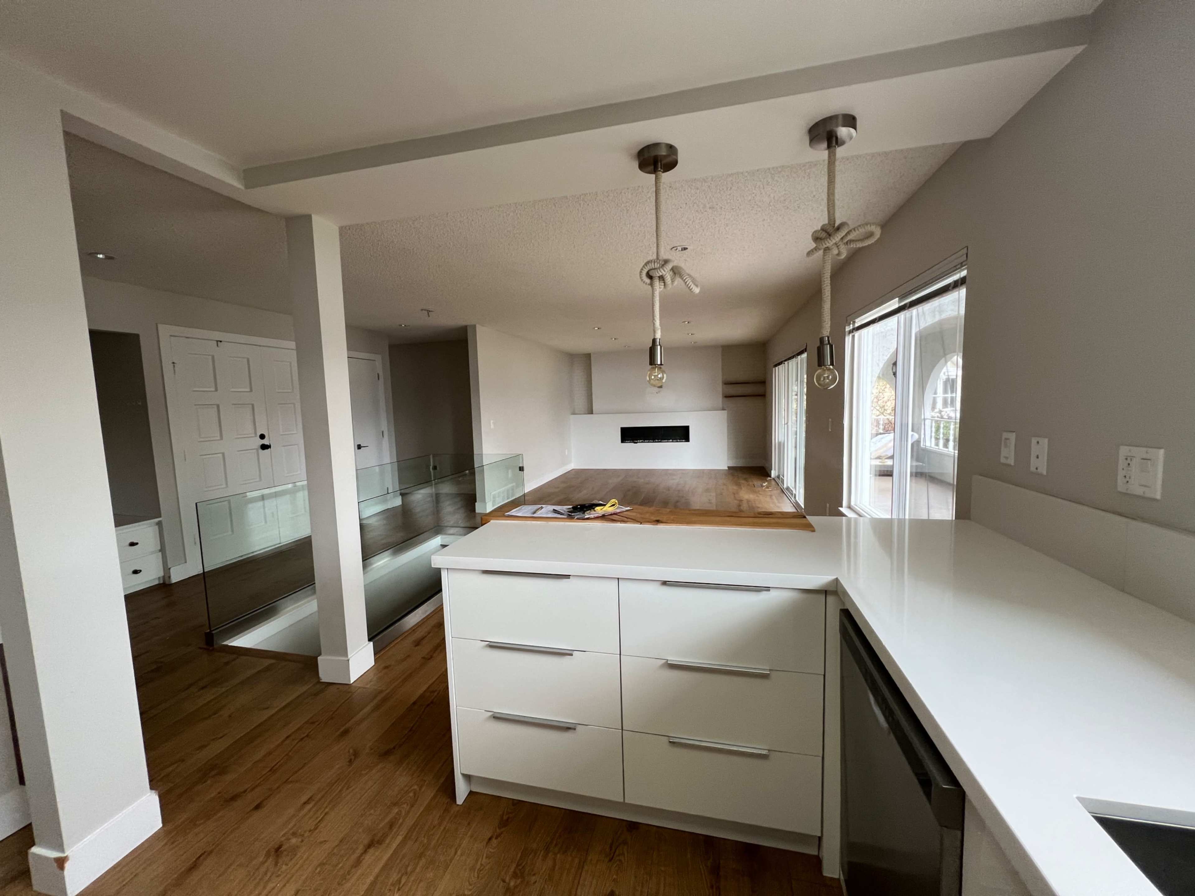 A modern kitchen with a central island, white cabinetry, and an open layout leading to a living area with large windows.