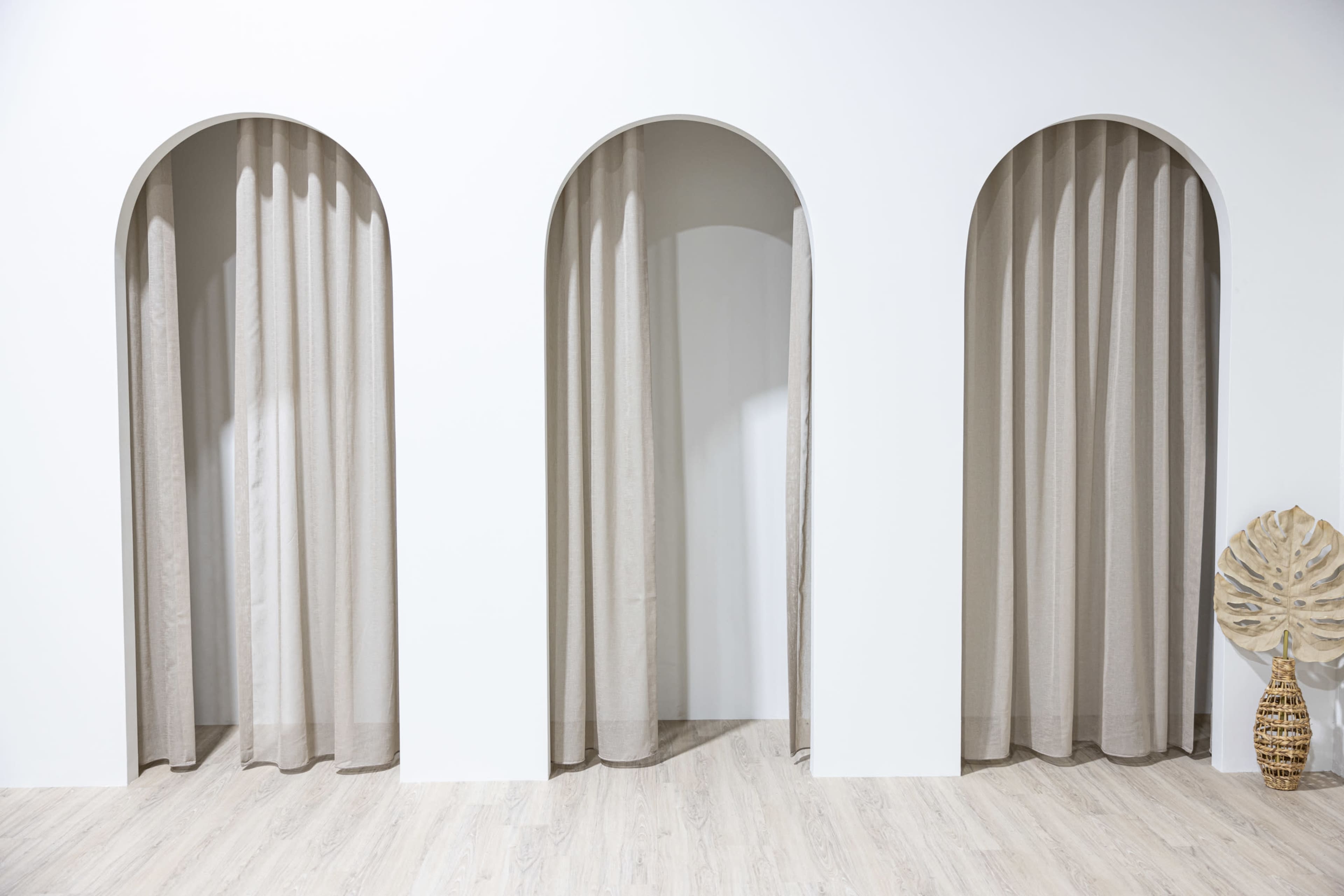 The image features three arched openings with neutral-colored curtains in a minimalist interior space.