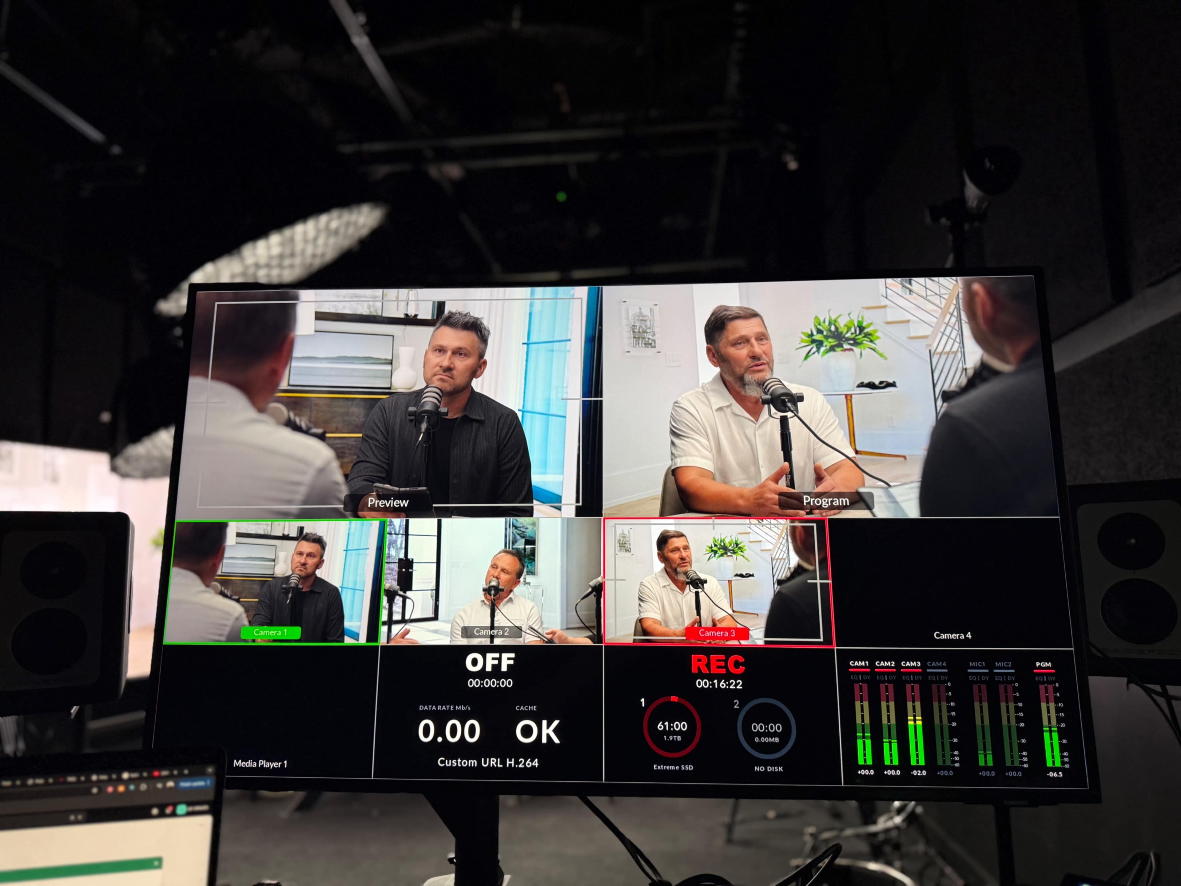 A camera setup displays a live podcast recording featuring two speakers in a studio setting.