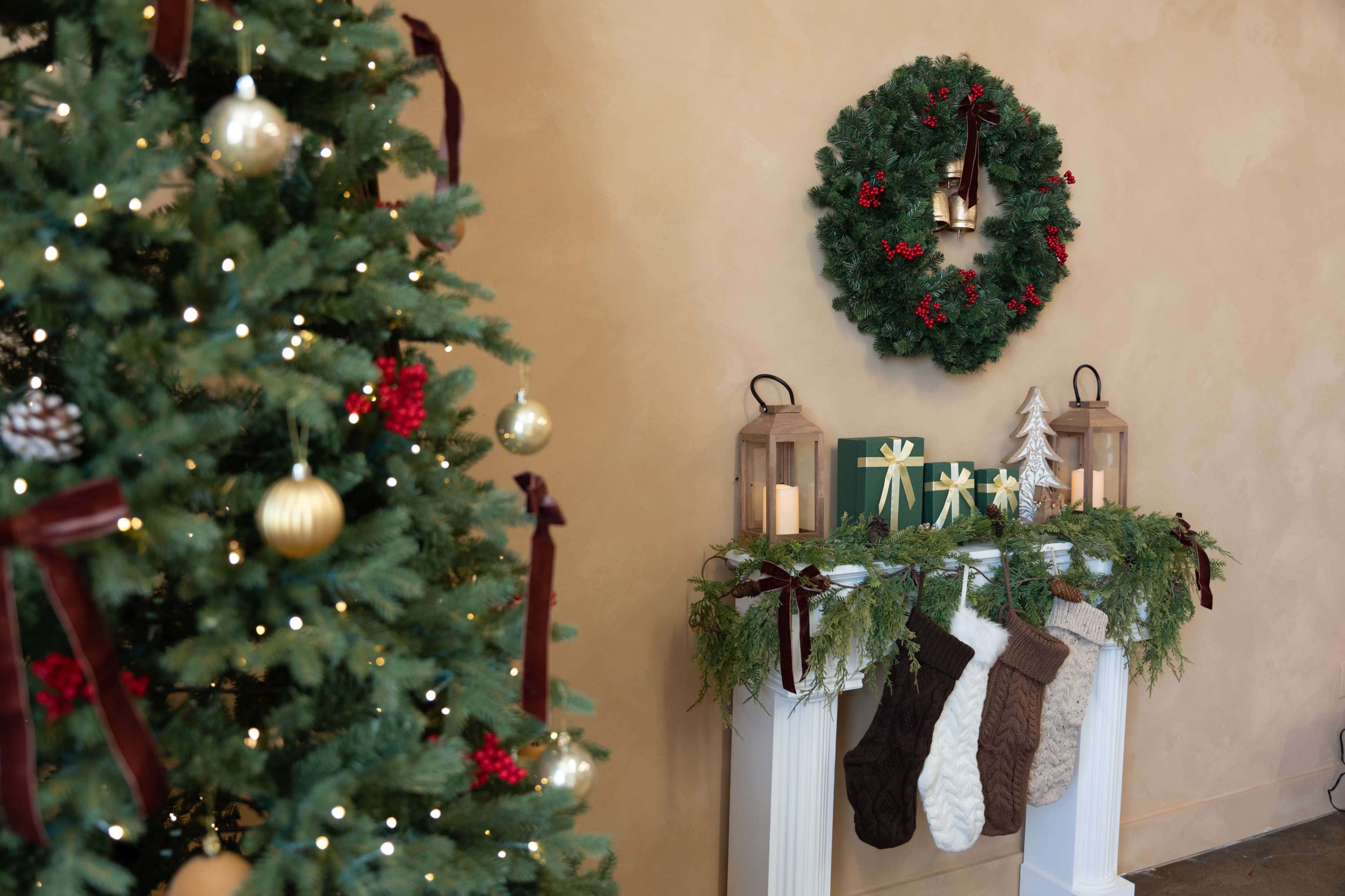 The image shows a decorated Christmas tree on the left and a mantel adorned with stockings, greenery, and lanterns on the right, with a wreath above.