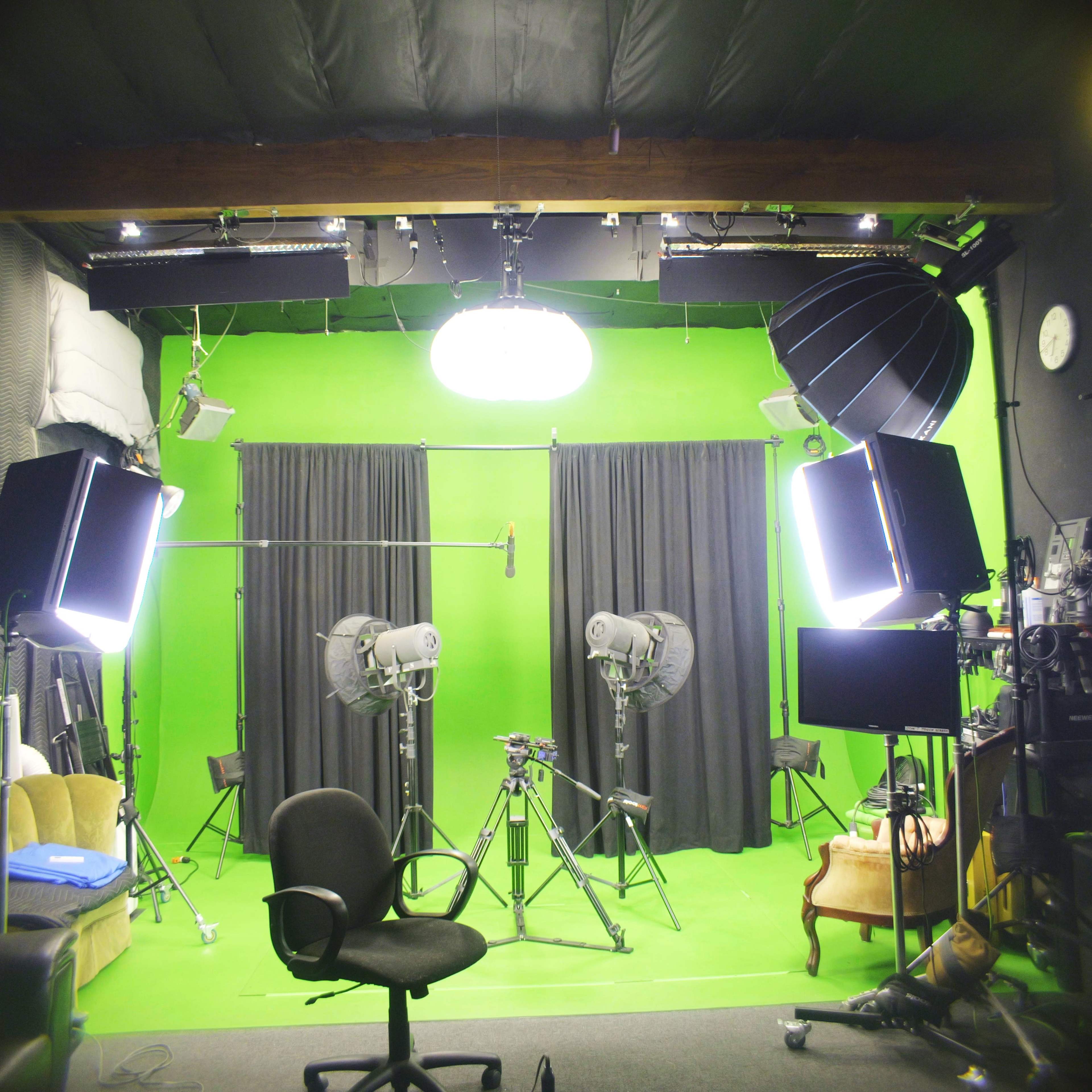 The image shows a green screen studio equipped with lighting, a microphone setup, and camera stands, with a chair positioned in front.