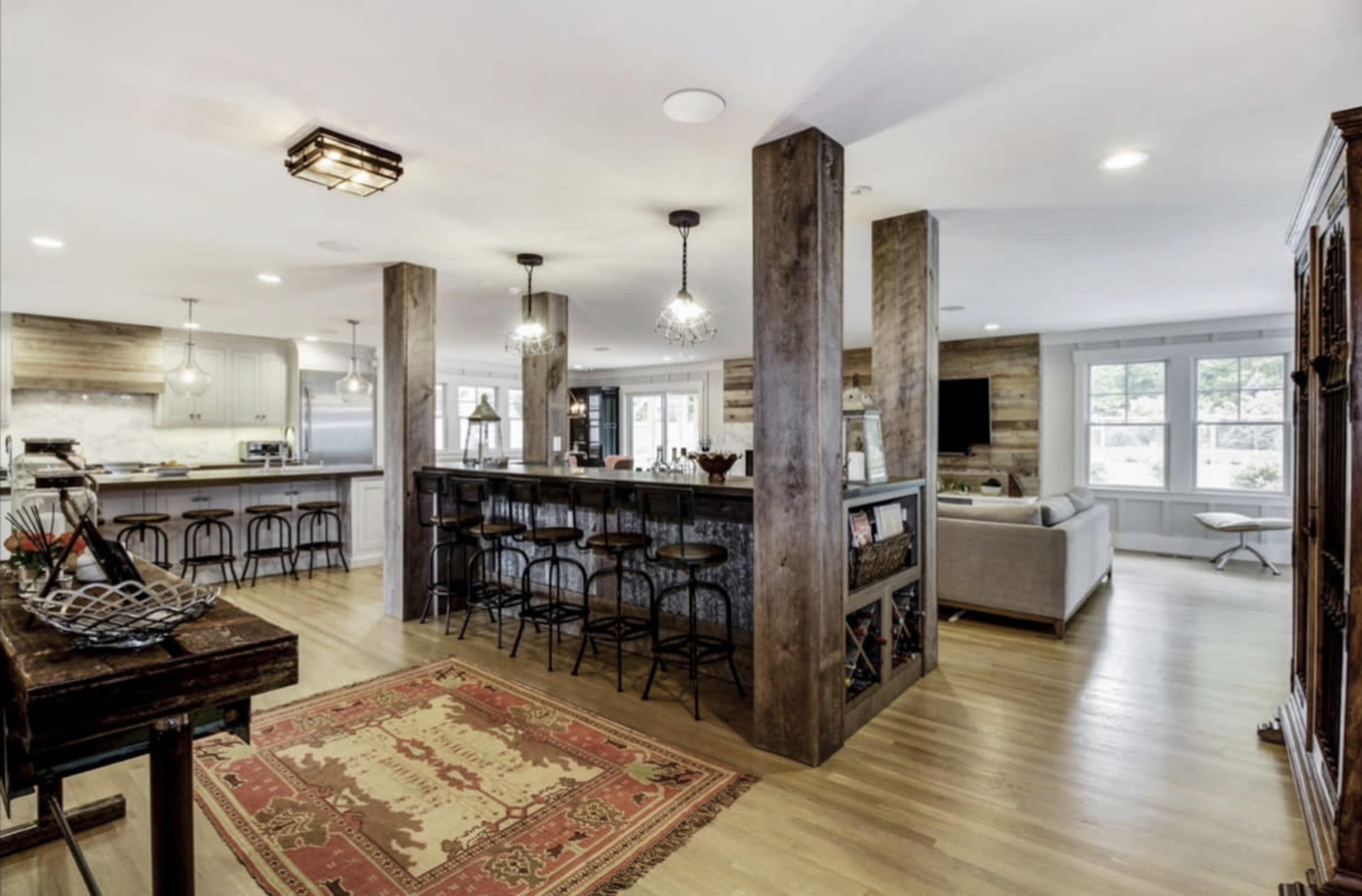 A modern kitchen and living area with wooden accents, a central island with bar seating, and large windows allowing natural light.