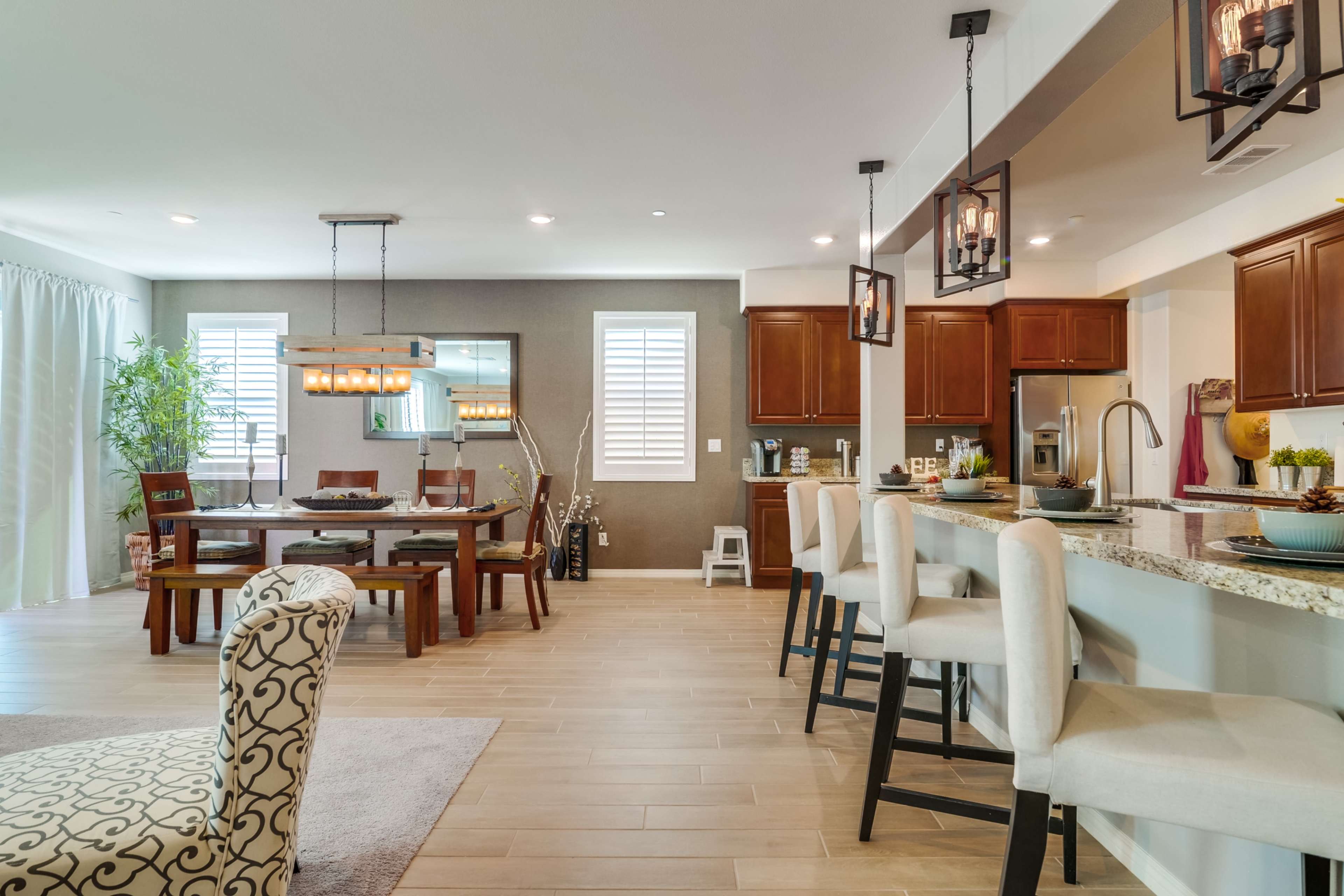 A modern open-concept kitchen and dining area featuring wooden cabinetry, a large dining table, and stylish bar stools.