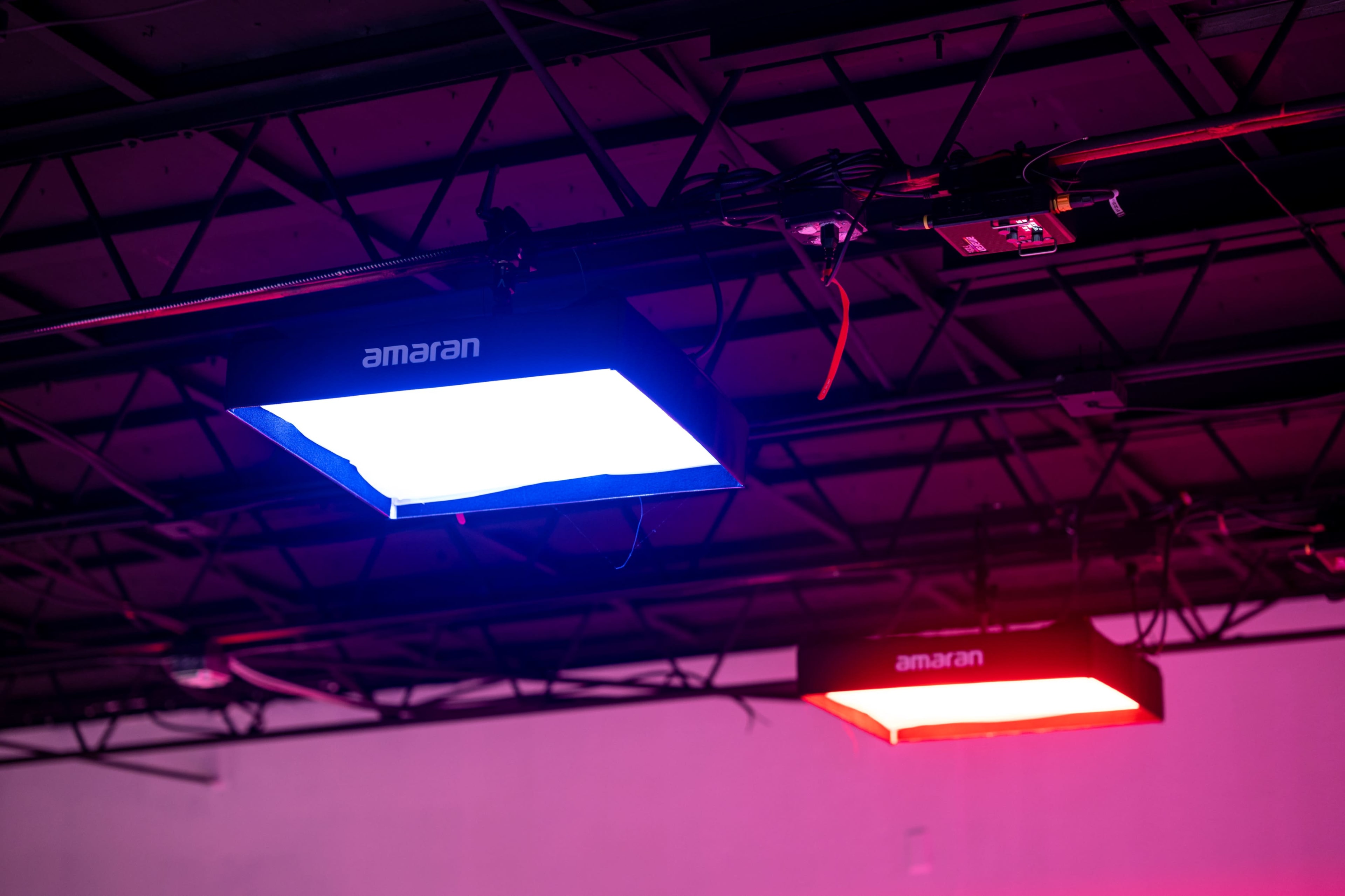 The image shows two rectangular lights mounted on a ceiling grid, one emitting a blue hue and the other a red hue.