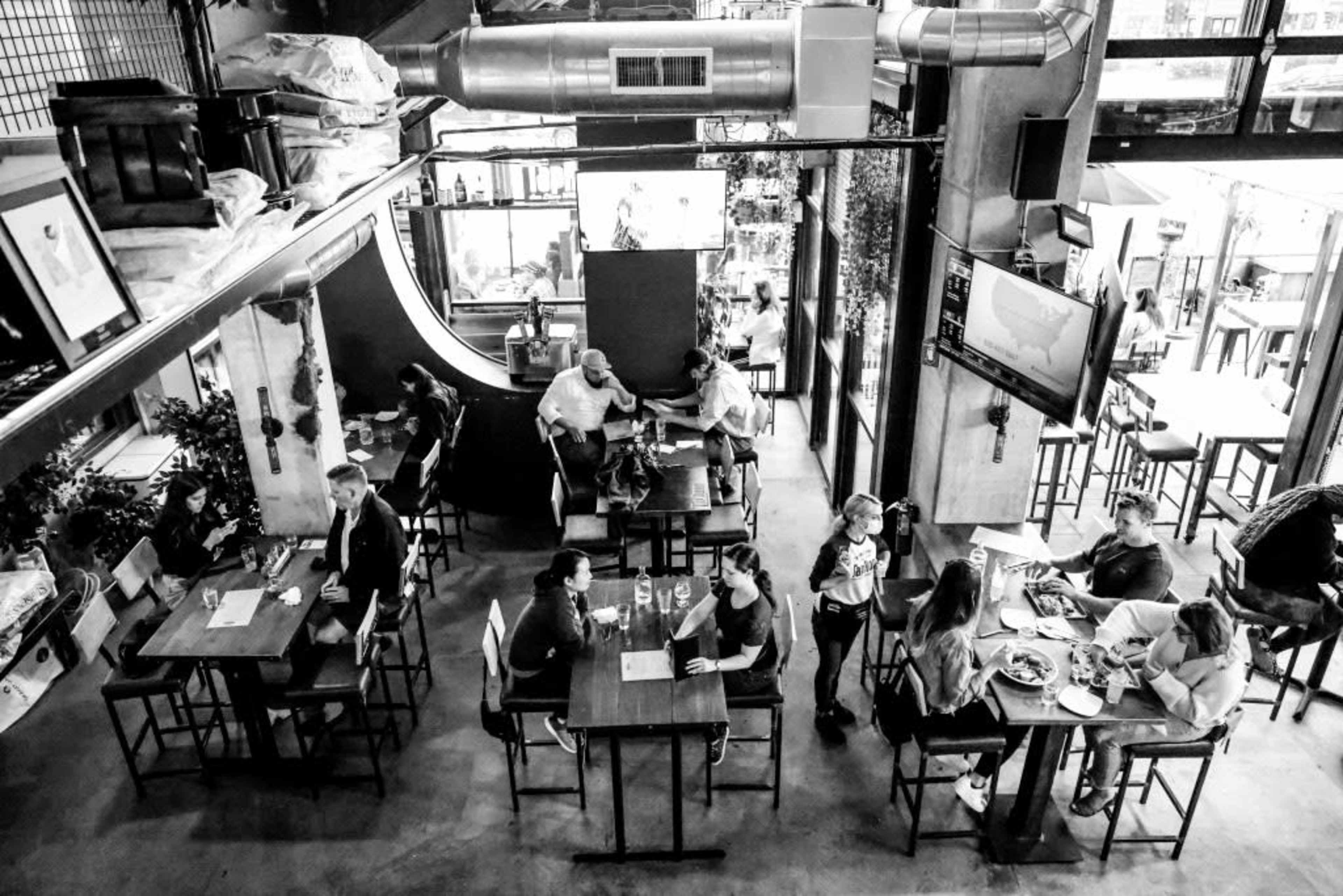 Aerial view of a busy restaurant with diners seated at tables and a mix of indoor plants and screens displaying information.