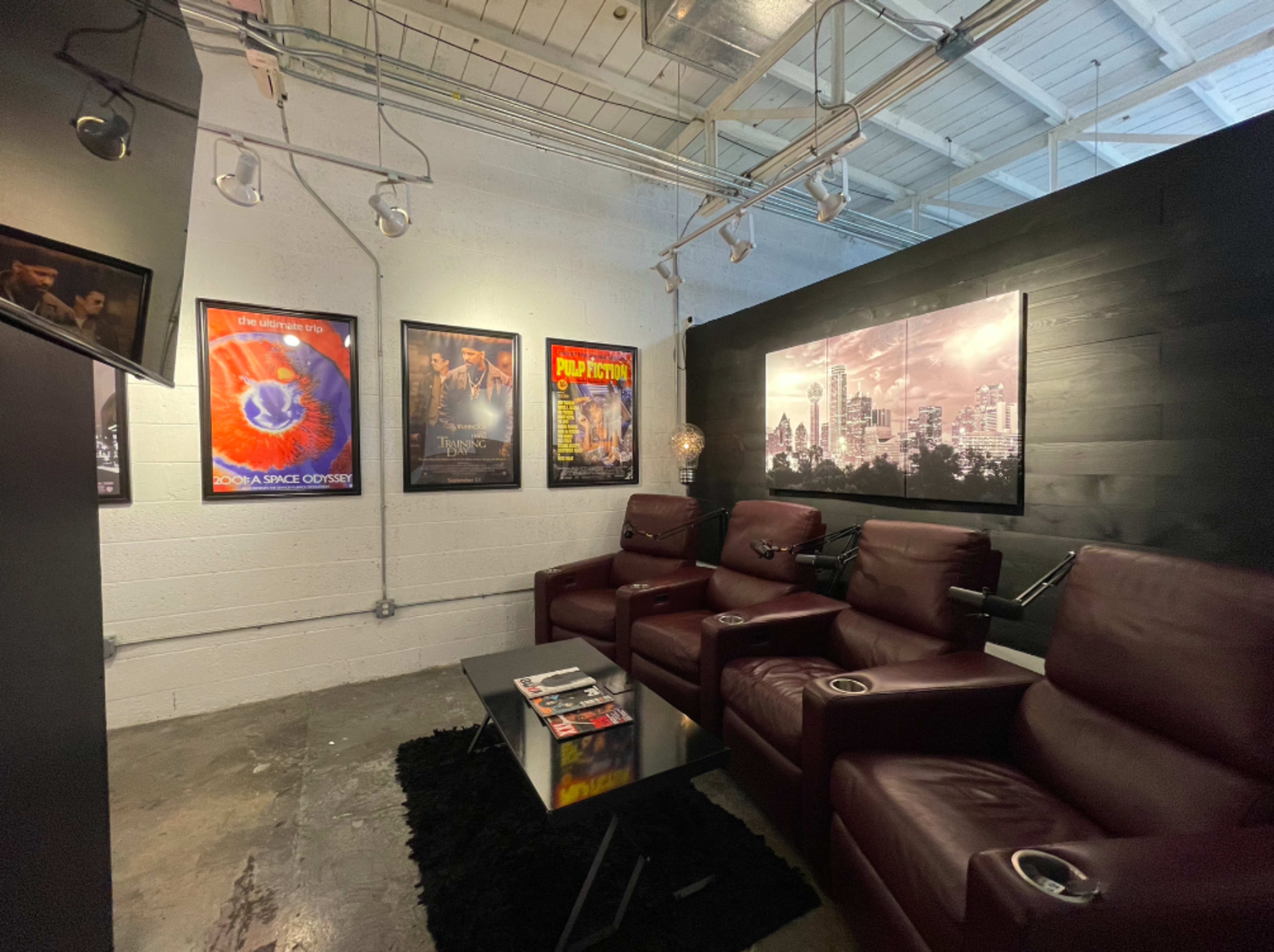 A home theater room featuring dark leather recliners arranged in front of a coffee table, with various movie posters displayed on the walls.