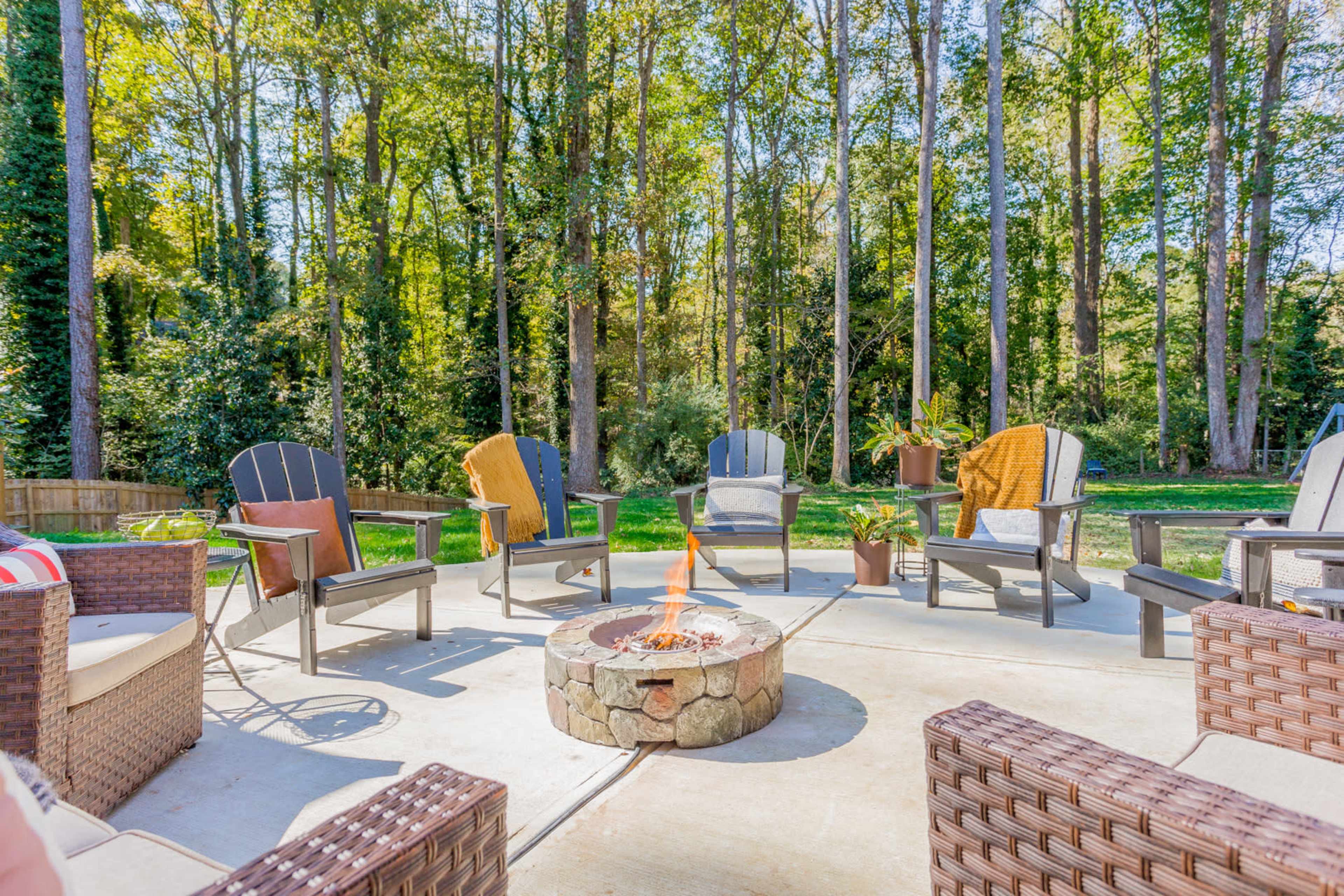 A stone fire pit surrounded by several outdoor chairs on a patio, with trees in the background.