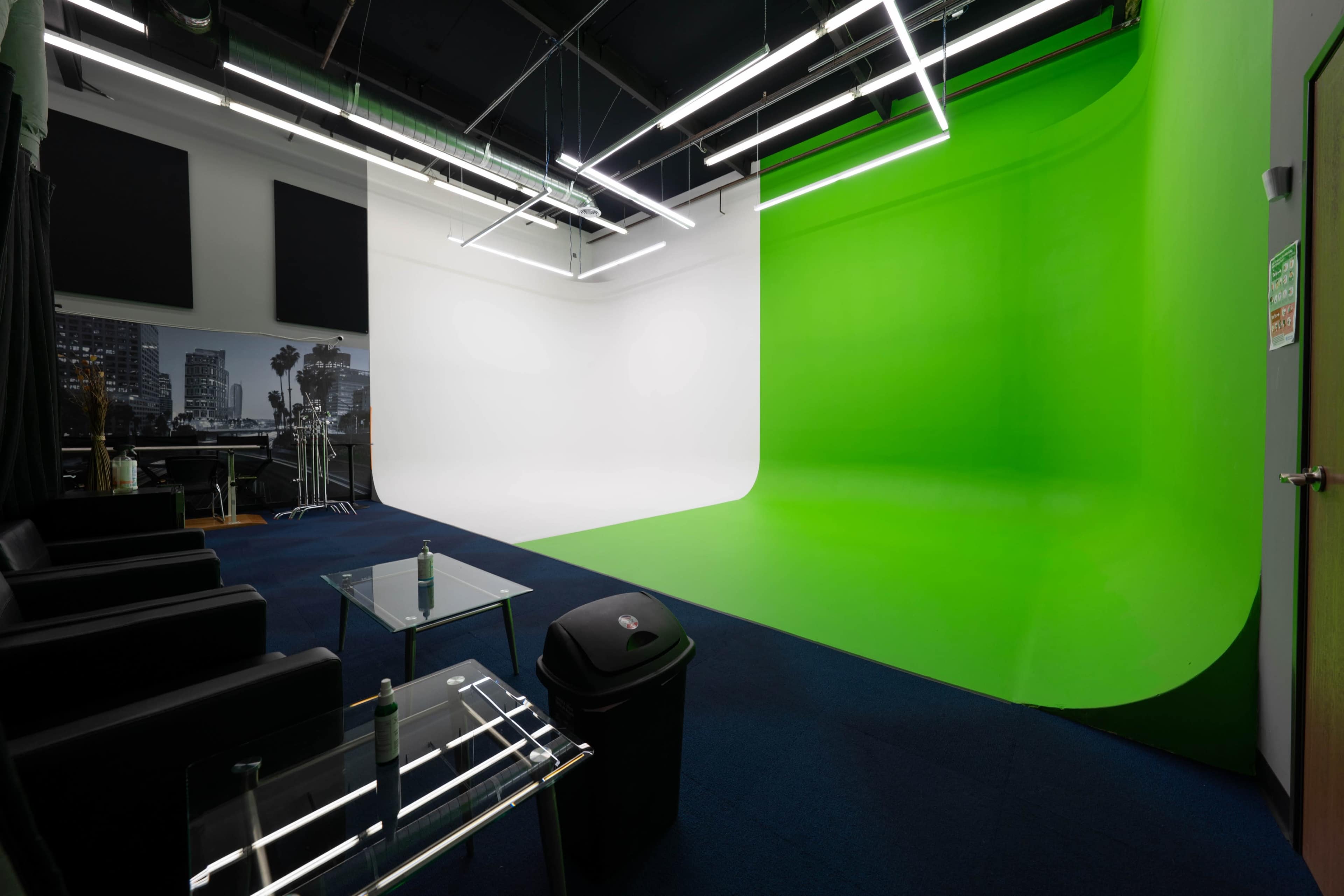 The image shows a studio with a green screen and a white backdrop, equipped with modern lighting and minimalist furnishings.