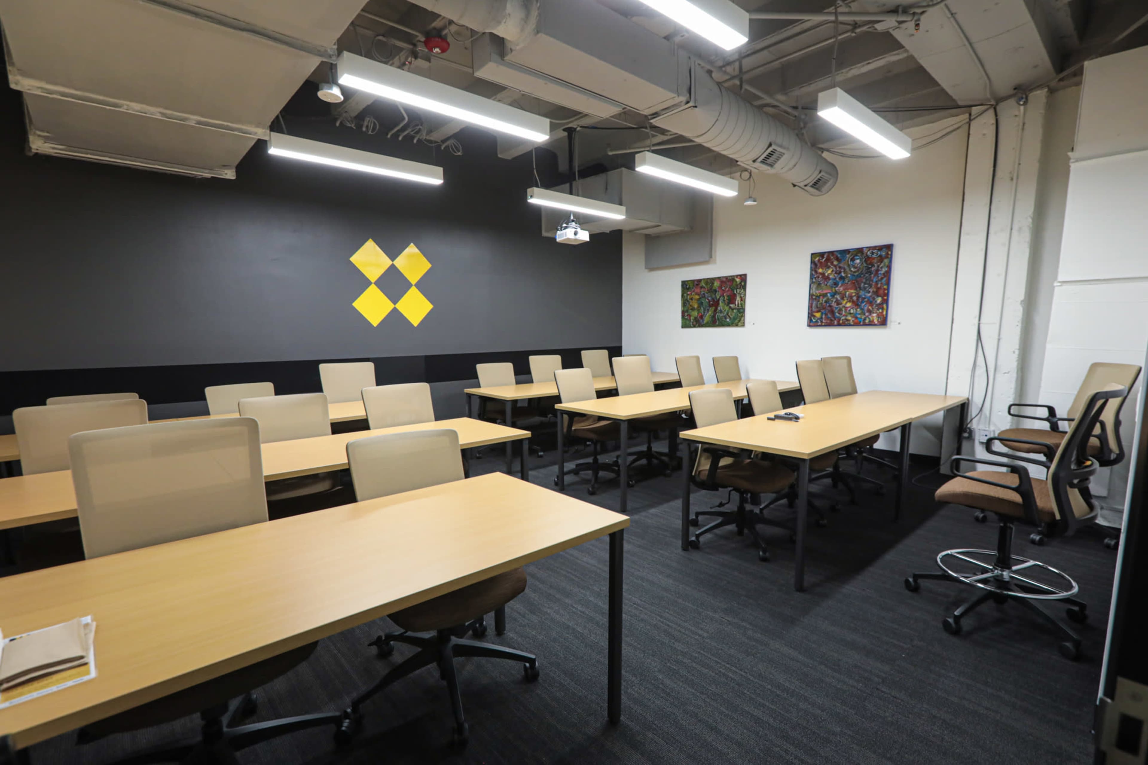 The image shows a modern meeting room with multiple rows of tables and chairs, and two artworks displayed on the wall.
