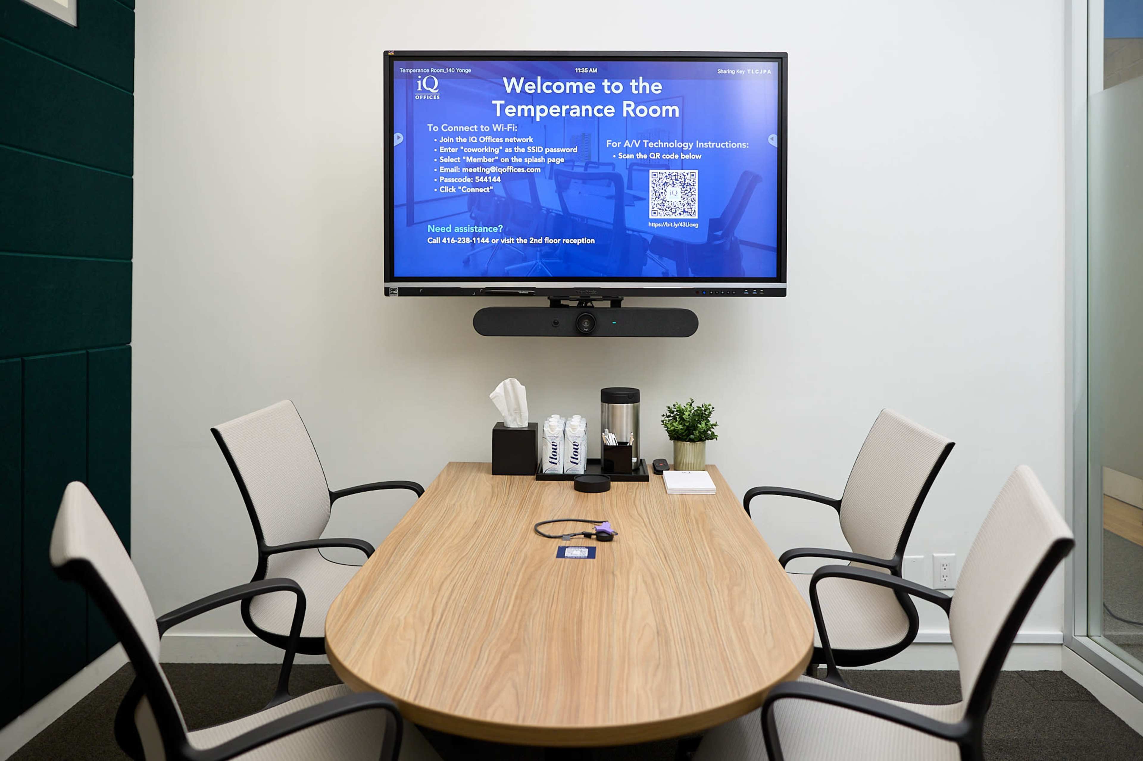 A conference room is shown with a large screen displaying instructions, a wooden oval table, and five chairs.