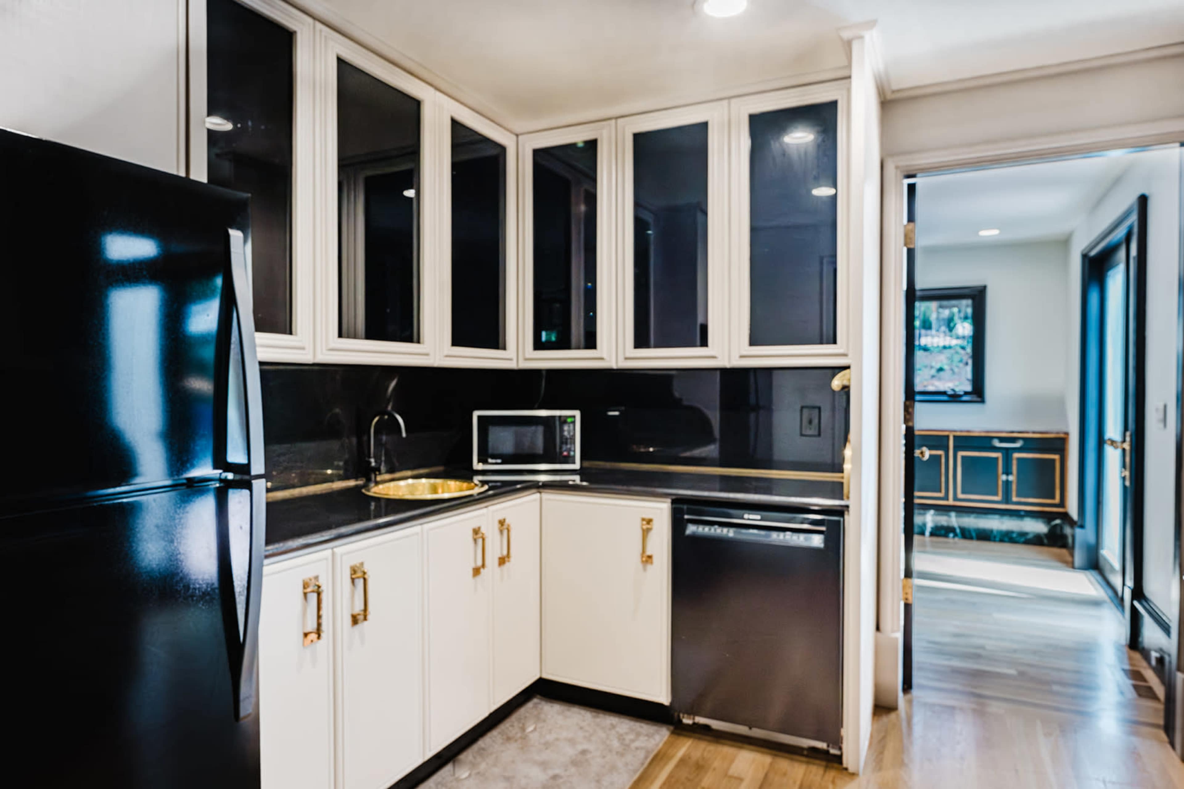 A modern kitchen features black appliances, white cabinetry with gold hardware, and a countertop with a sink and microwave.