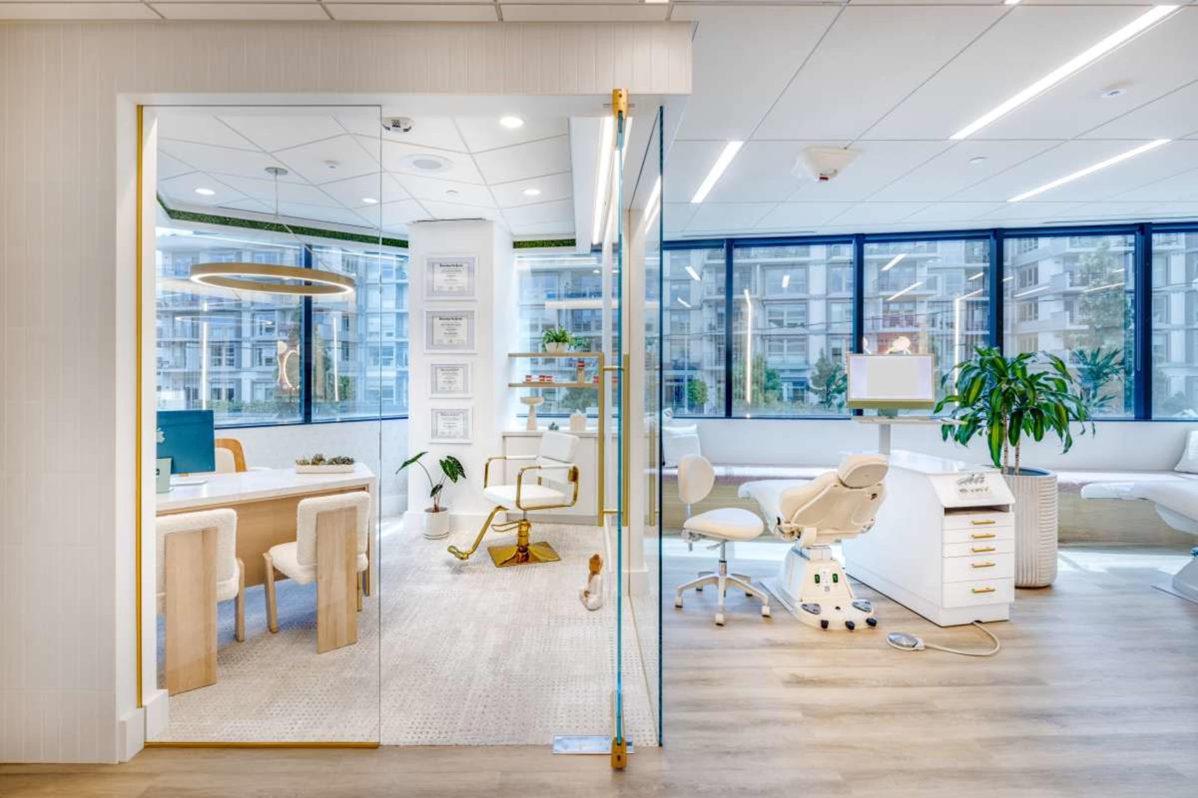 The image shows a modern office space divided by a glass wall, featuring a reception area with a desk and chairs on one side and a dental treatment area with equipment on the other.