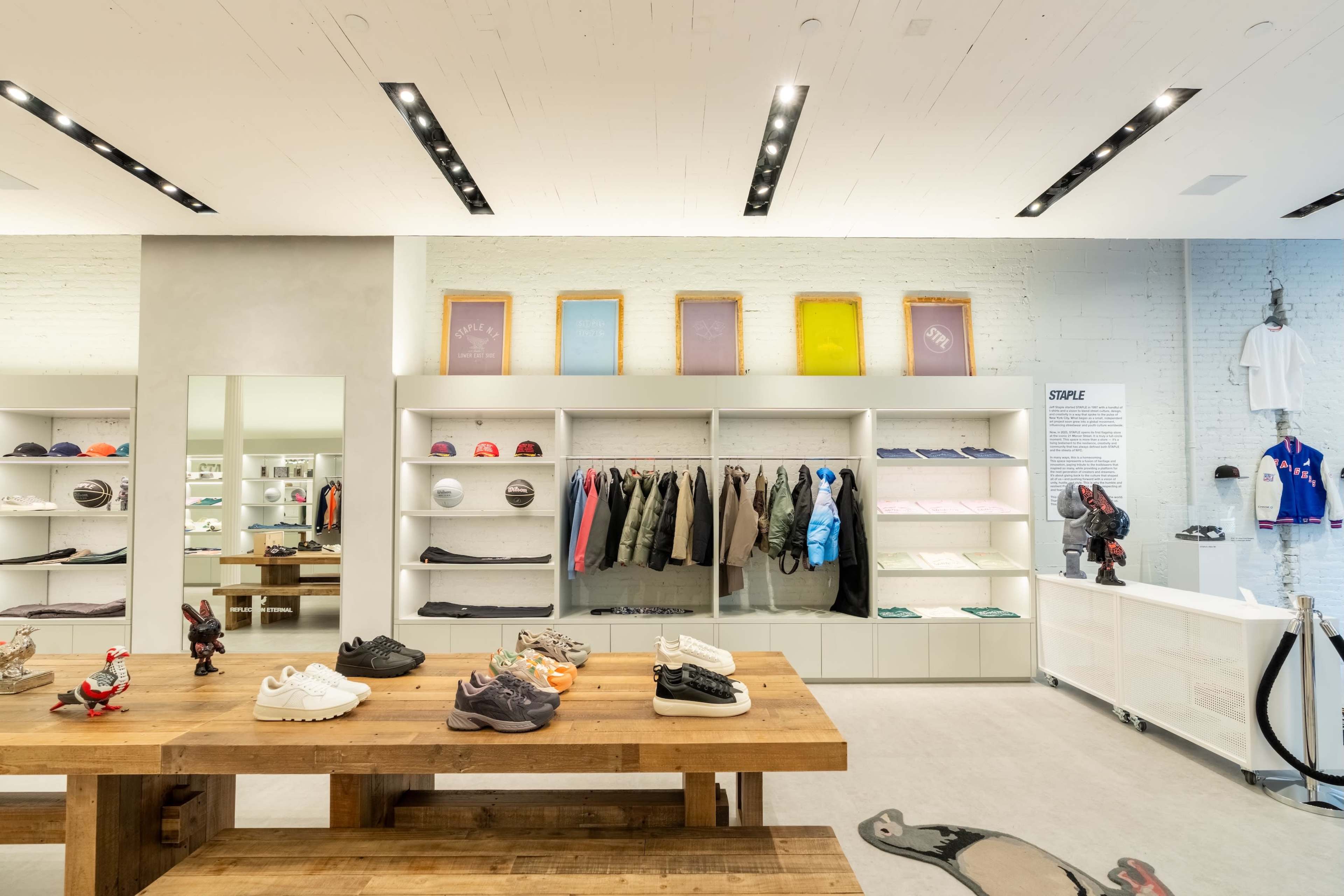 The image shows a modern retail store interior with a wooden display table, shelving units, and various clothing and sneaker items on display.
