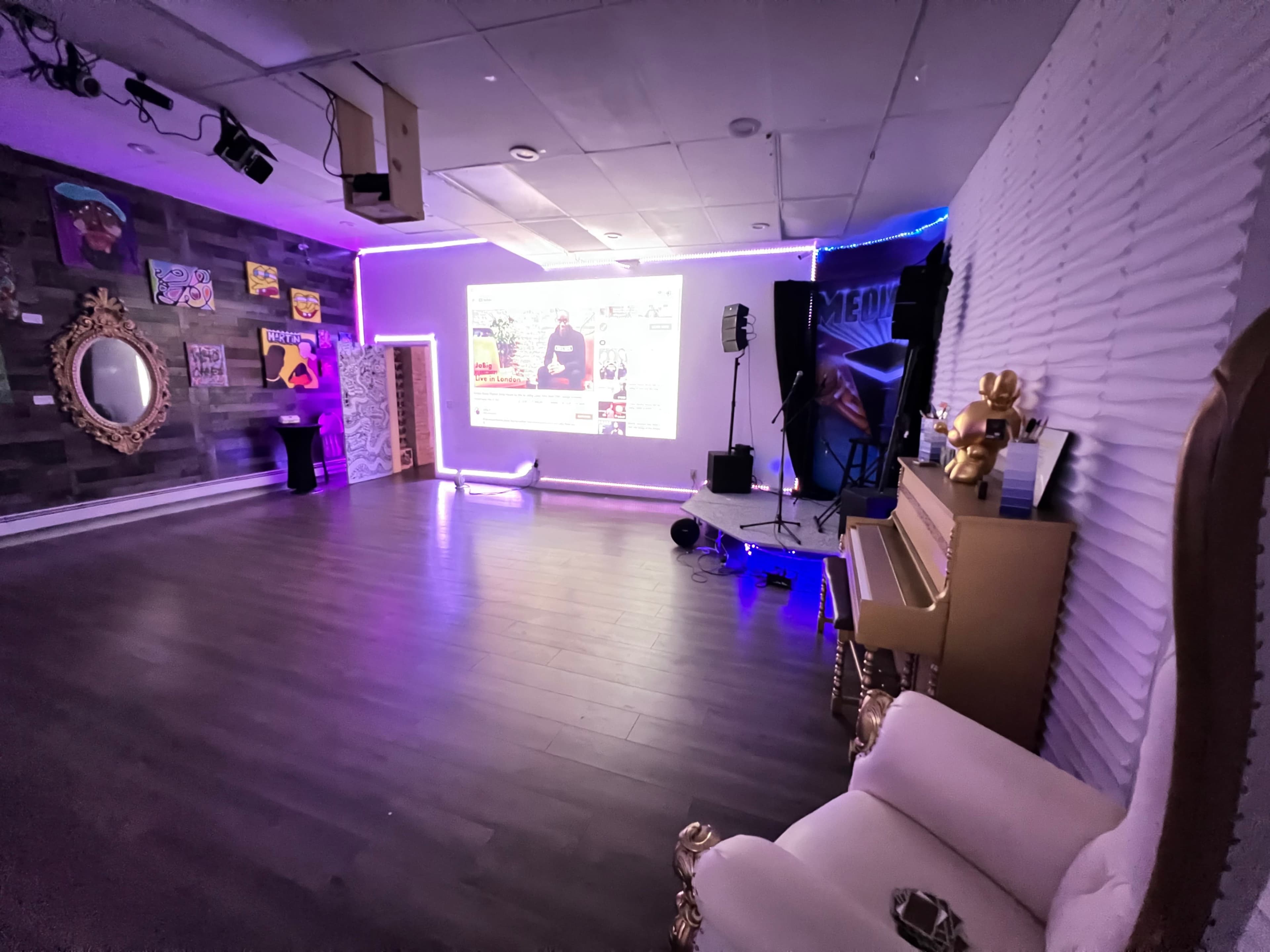 A modern event space with purple lighting, a piano, and a screen displaying a video.