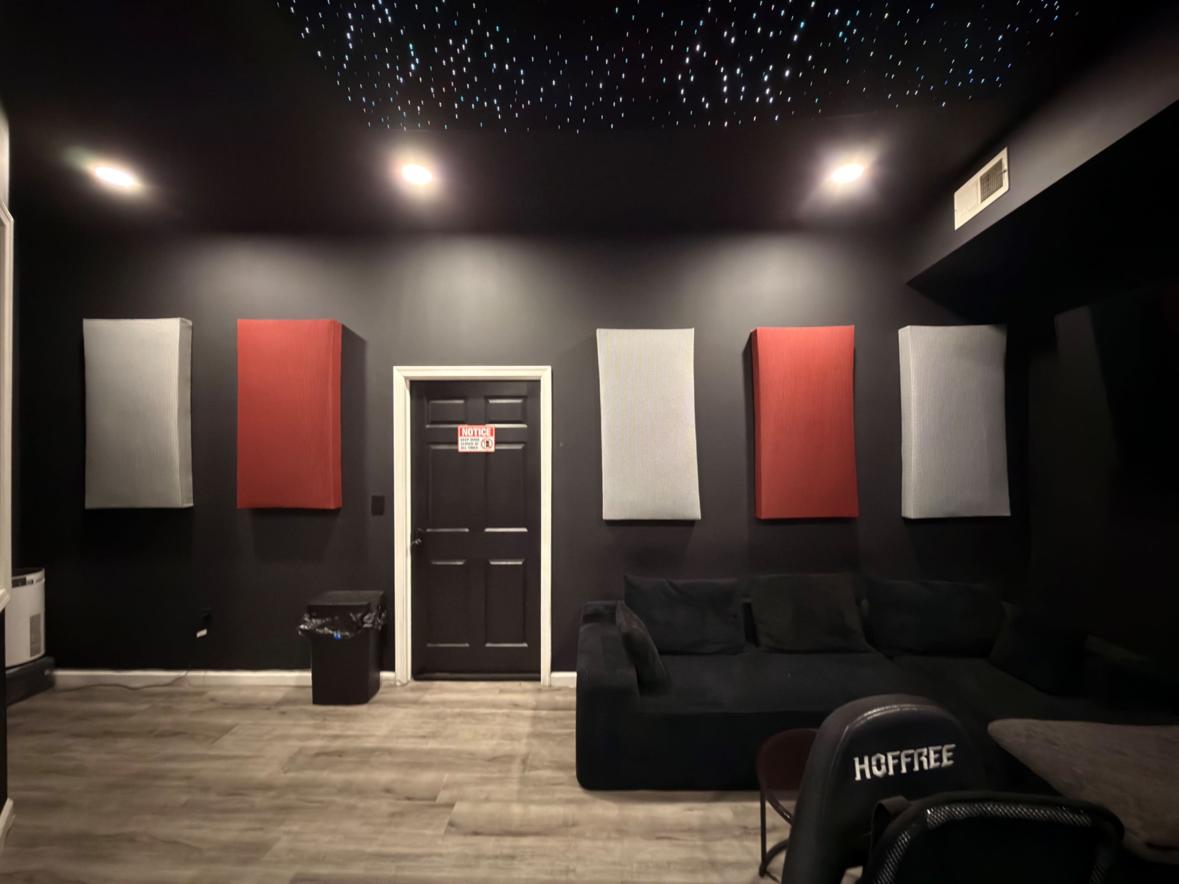 The image shows a soundproofed room with dark walls, a couch, four wall panels, and a closed door, illuminated by ceiling lights resembling stars.