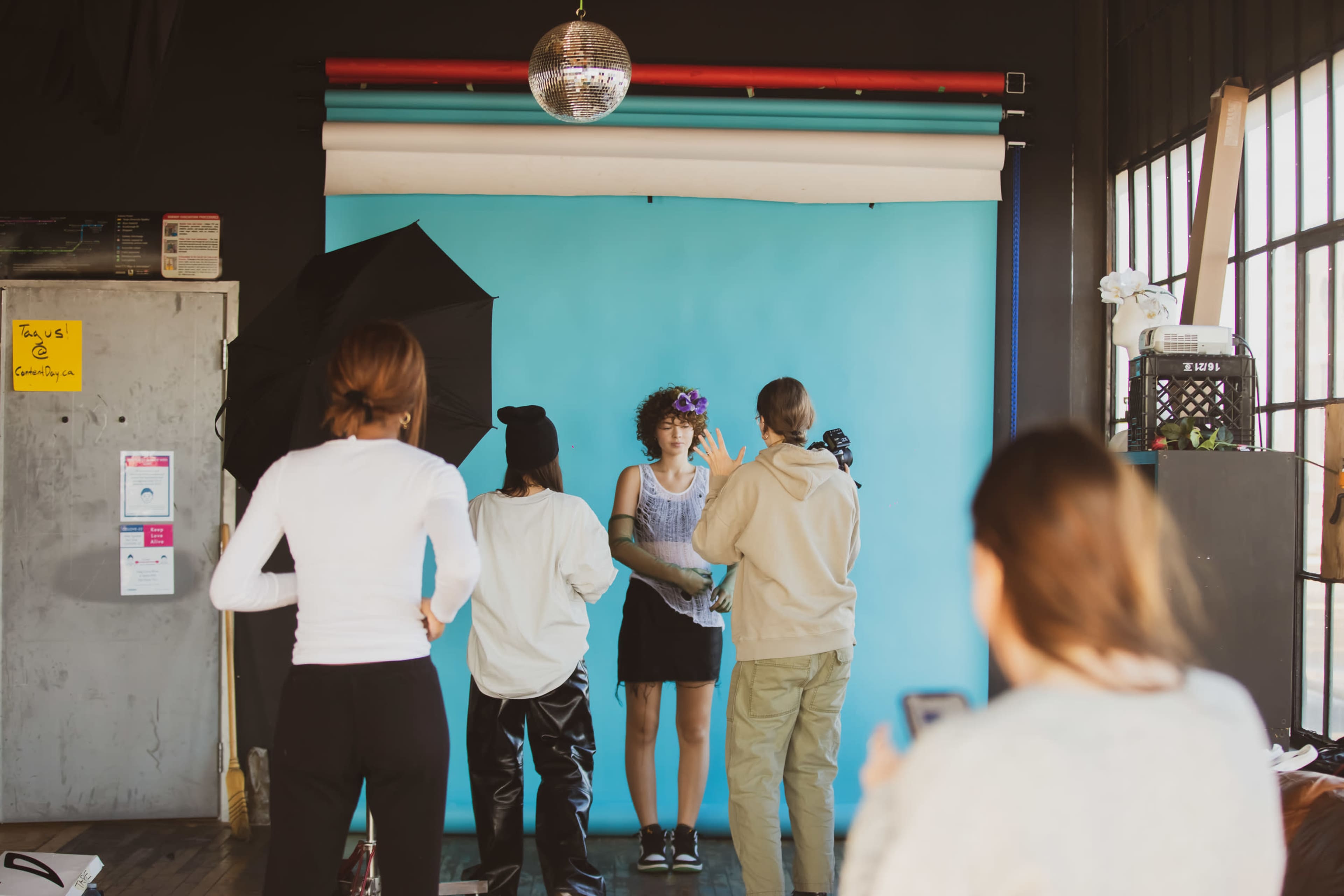 A model poses in front of a blue backdrop while photographers and assistants prepare for a photoshoot in a studio setting.