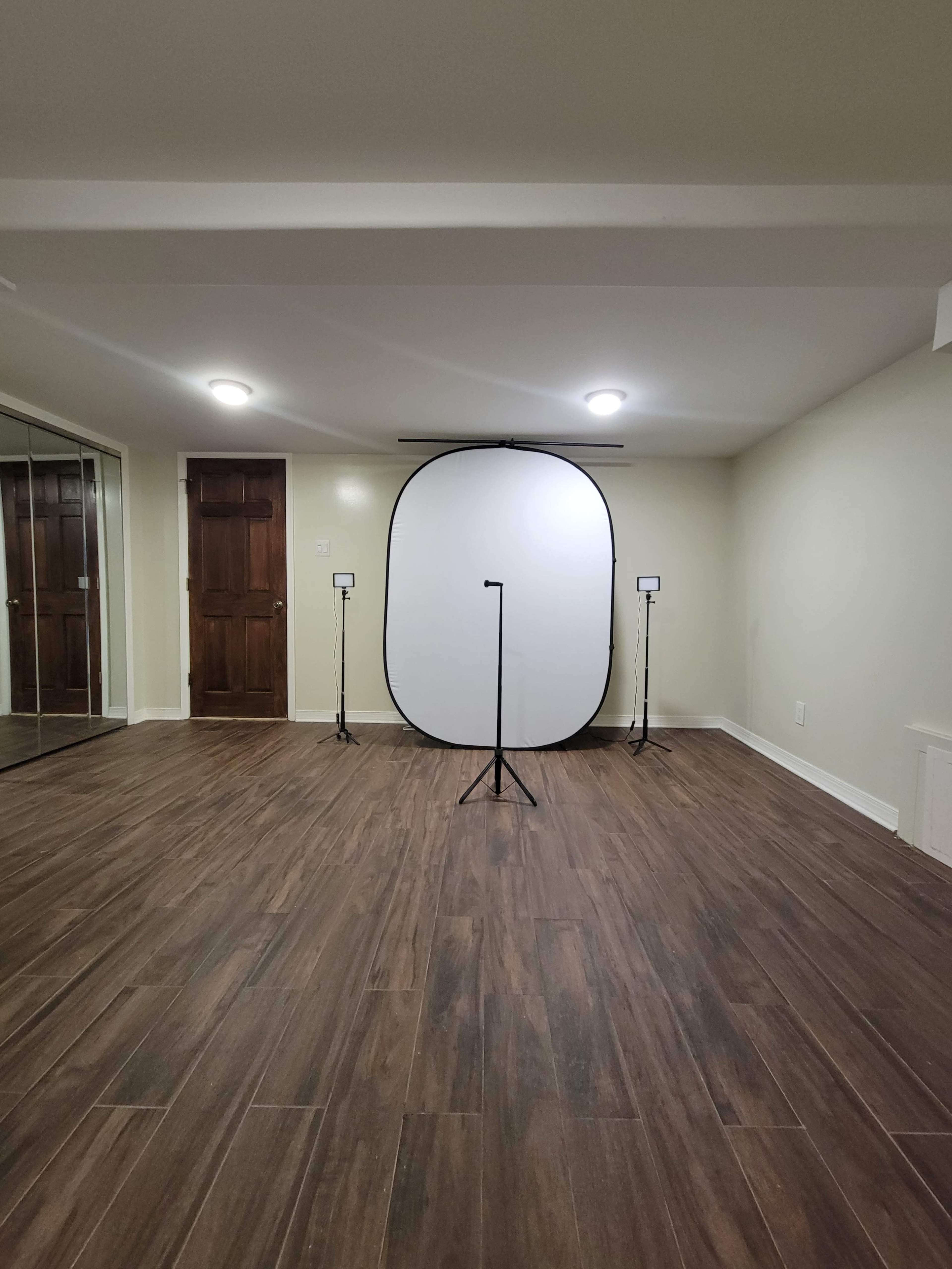 An empty room with a wooden floor features a freestanding backdrop supported by a stand, flanked by two lights on either side.