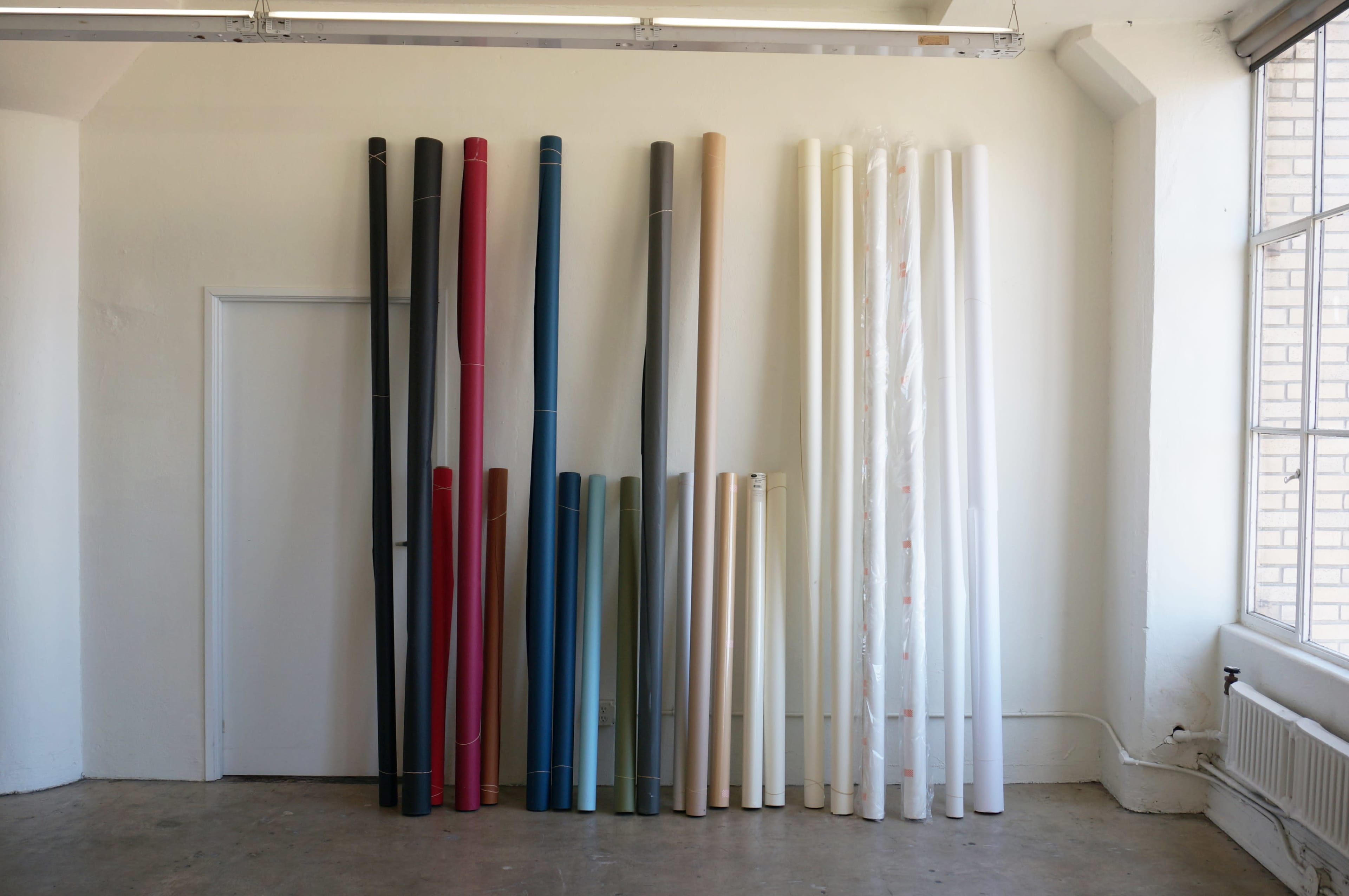 A collection of neatly arranged rolls of colored paper and fabric are displayed against a wall in a well-lit room.