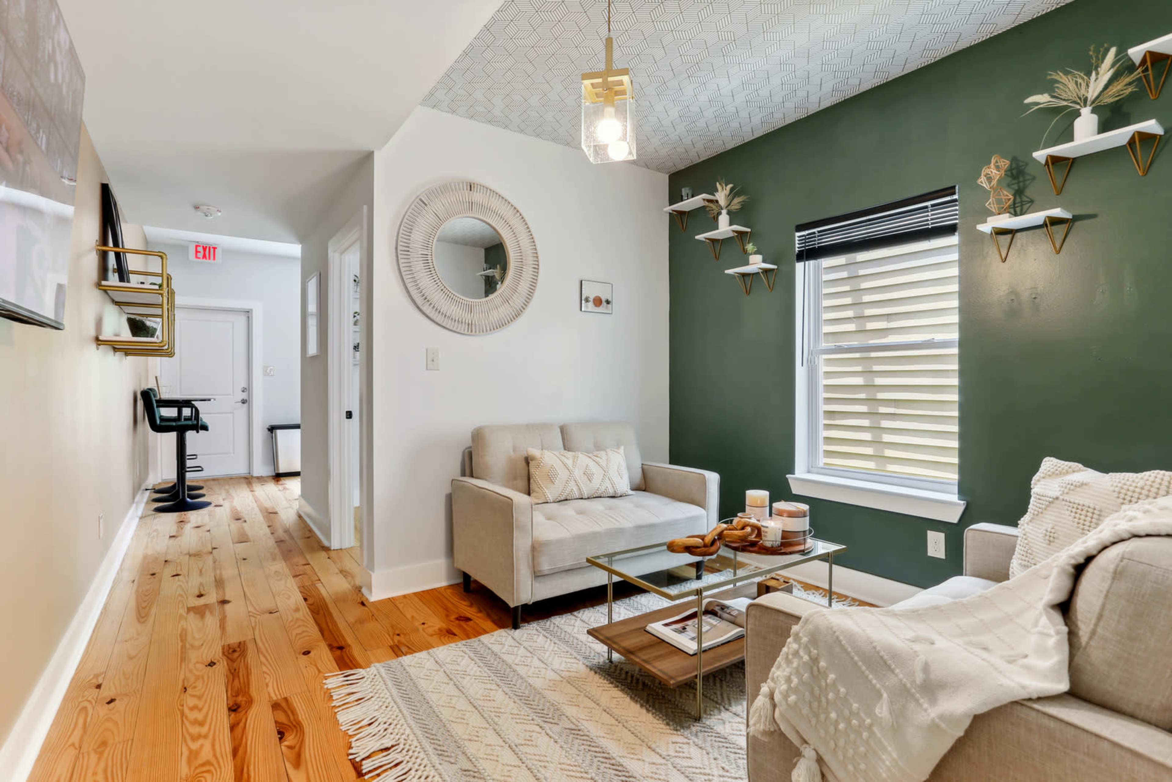 A living room features two light-colored sofas, a glass coffee table, and green accent walls, with decorative shelves and natural wood flooring.